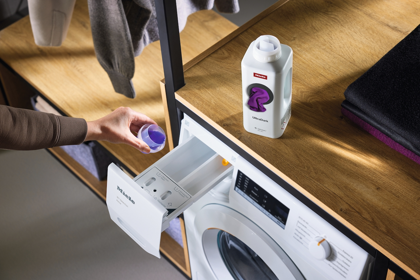 Eine Hand gießt lila Waschmittel in die Waschmittelschublade einer Miele-Waschmaschine.