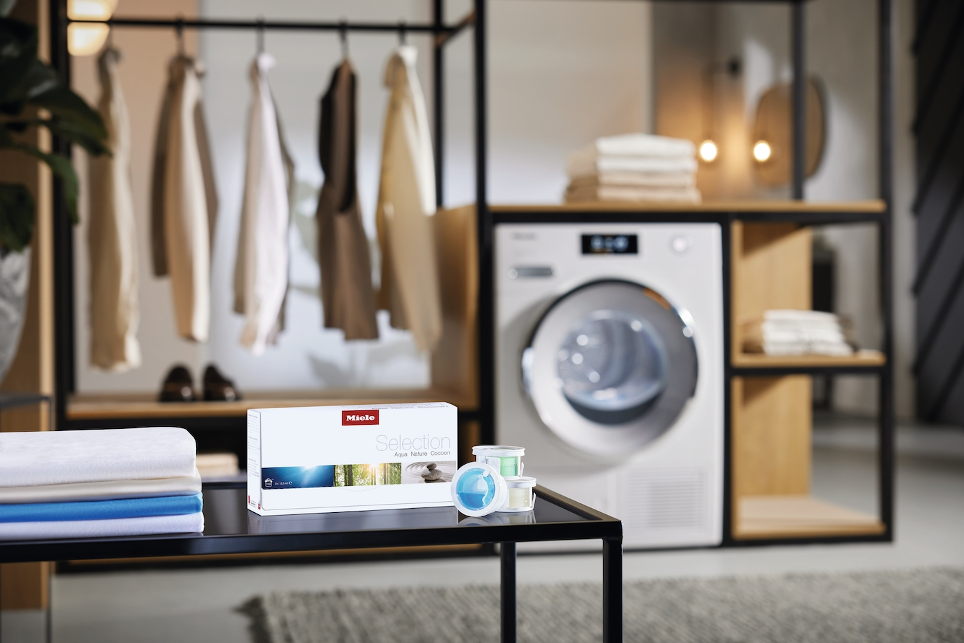 Miele Waschmittelbox und Spender stehen auf einem Tisch vor einer Waschmaschine.