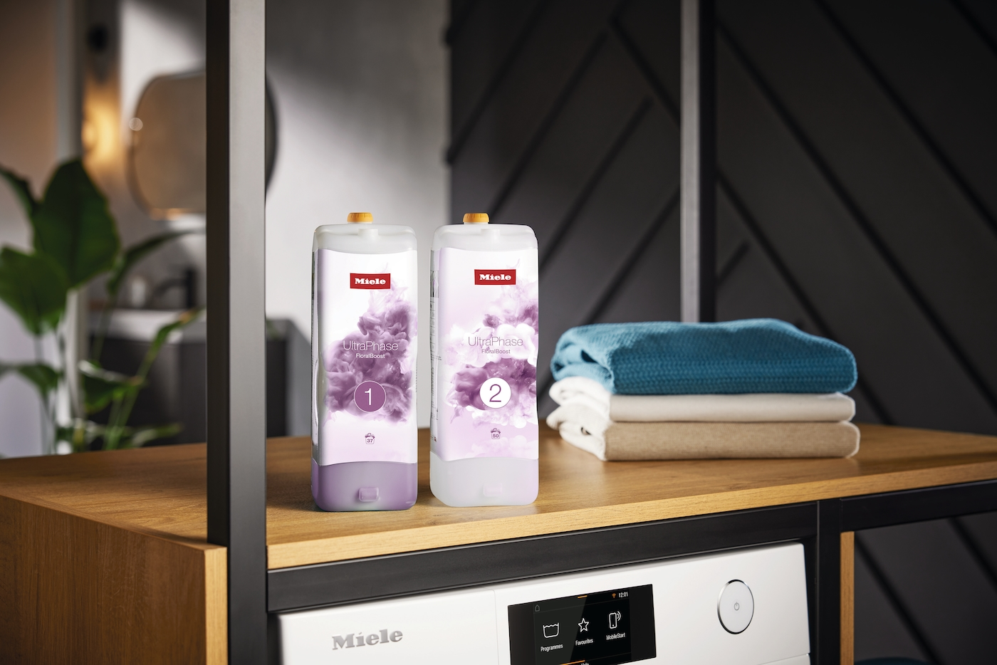 Zwei Miele UltraPhase Flaschen und gefaltete Wäsche auf einem Holztisch.