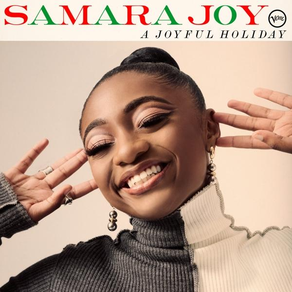 Samara Joy lächelt, trägt einen Rollkragenpullover. Der Hintergrund hat einen Text: A Joyful Holiday. Roter und grüner Text.