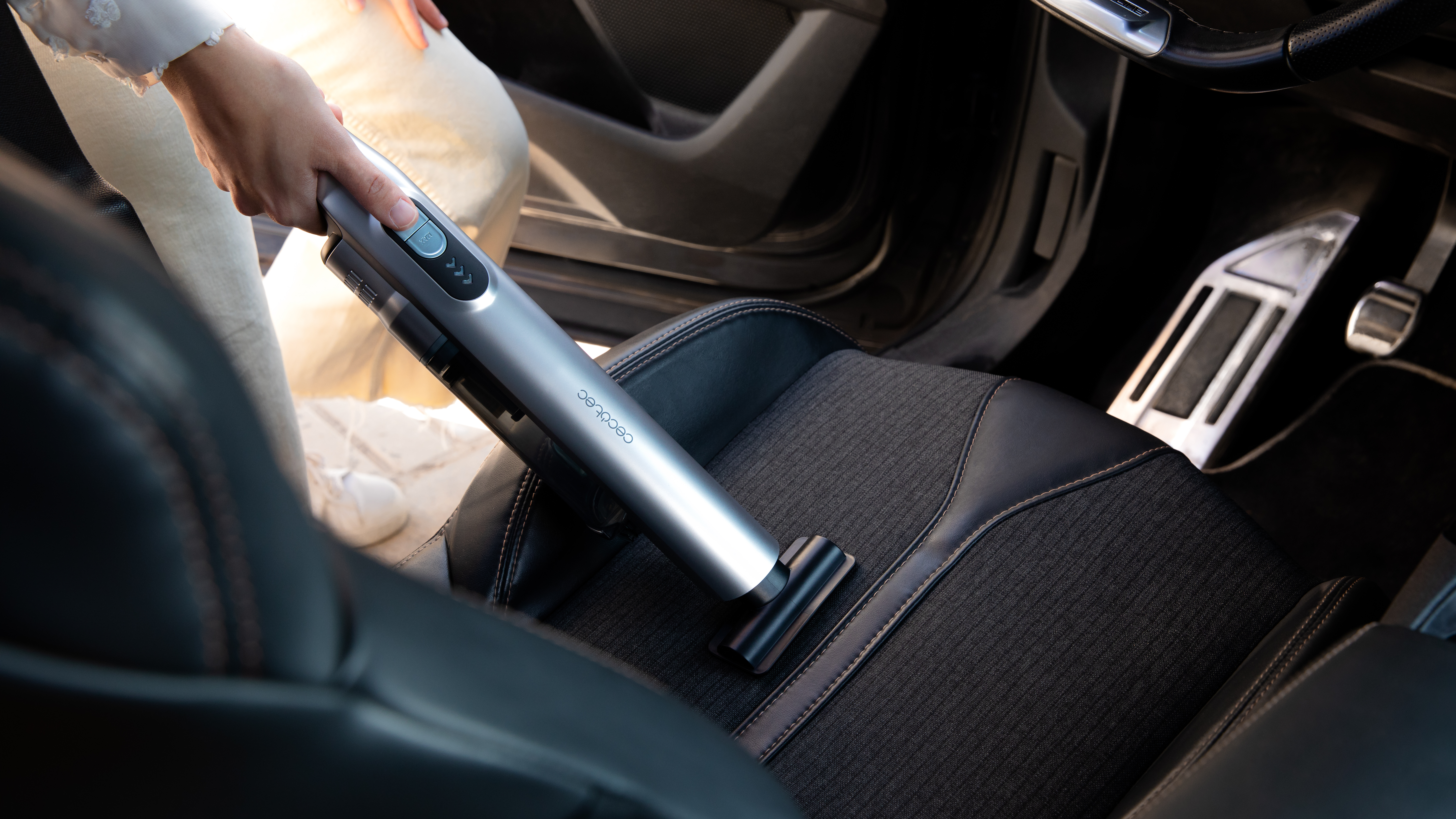 Persona aspirando un asiento de coche con una aspiradora de mano.