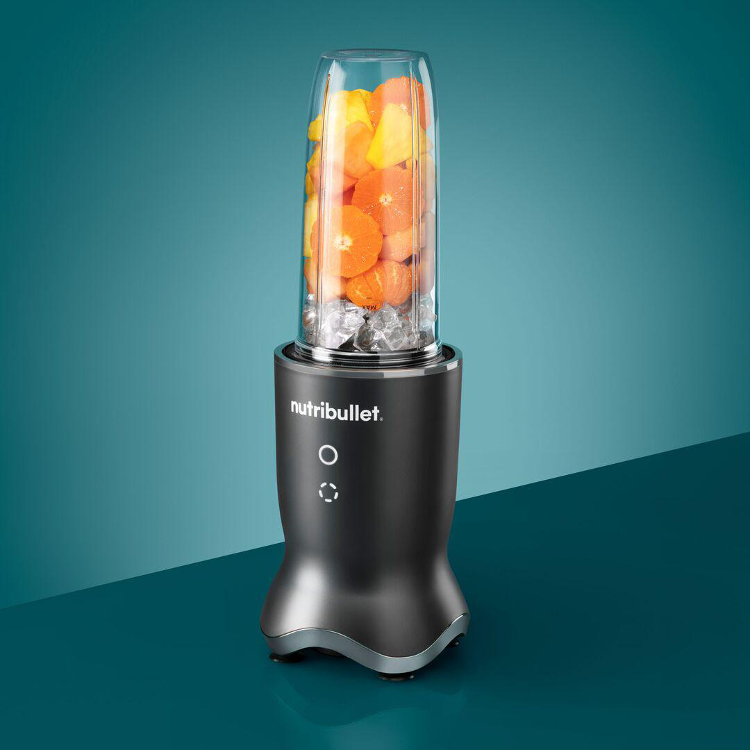 Ein schwarzer Mixer gefüllt mit orangefarbenen und gelben Früchten, auf blauer Oberfläche.