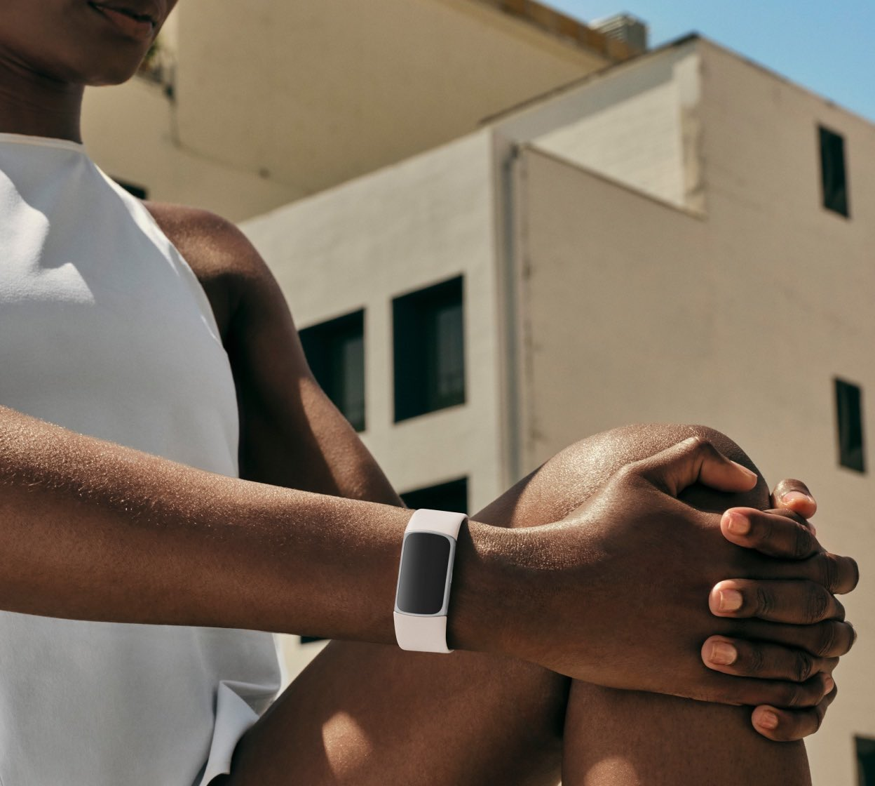 Donna con orologio fitness tracker bianco al polso, seduta fuori, vicino a un edificio.