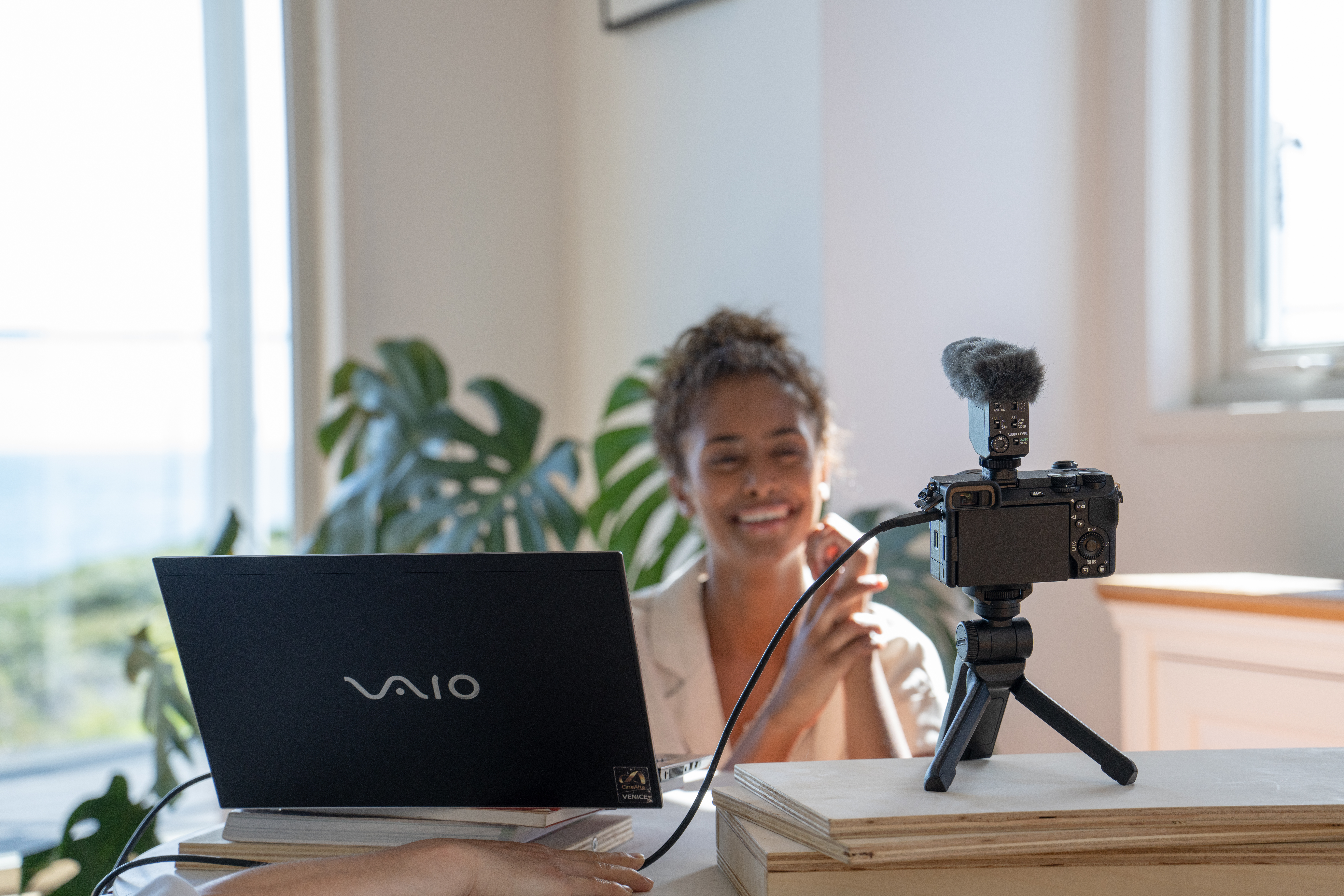 Donna che fa vlogging con laptop, fotocamera e microfono su una scrivania.