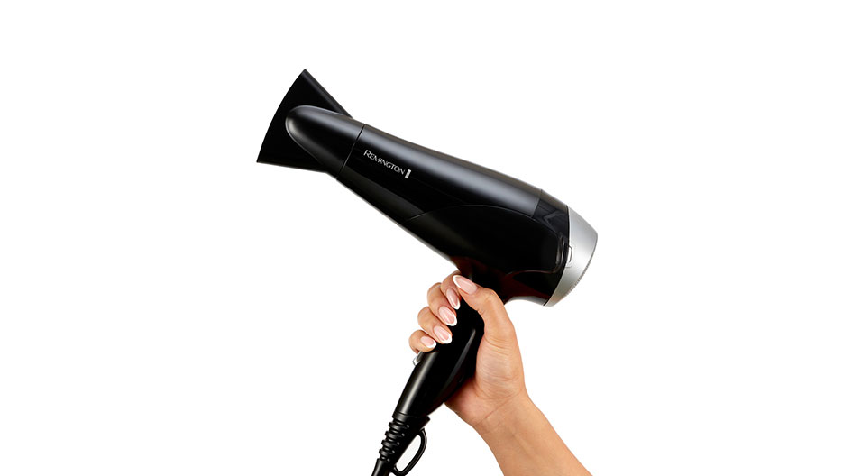 Kéz tartja a fekete Remington hajszárítót fehér háttéren.