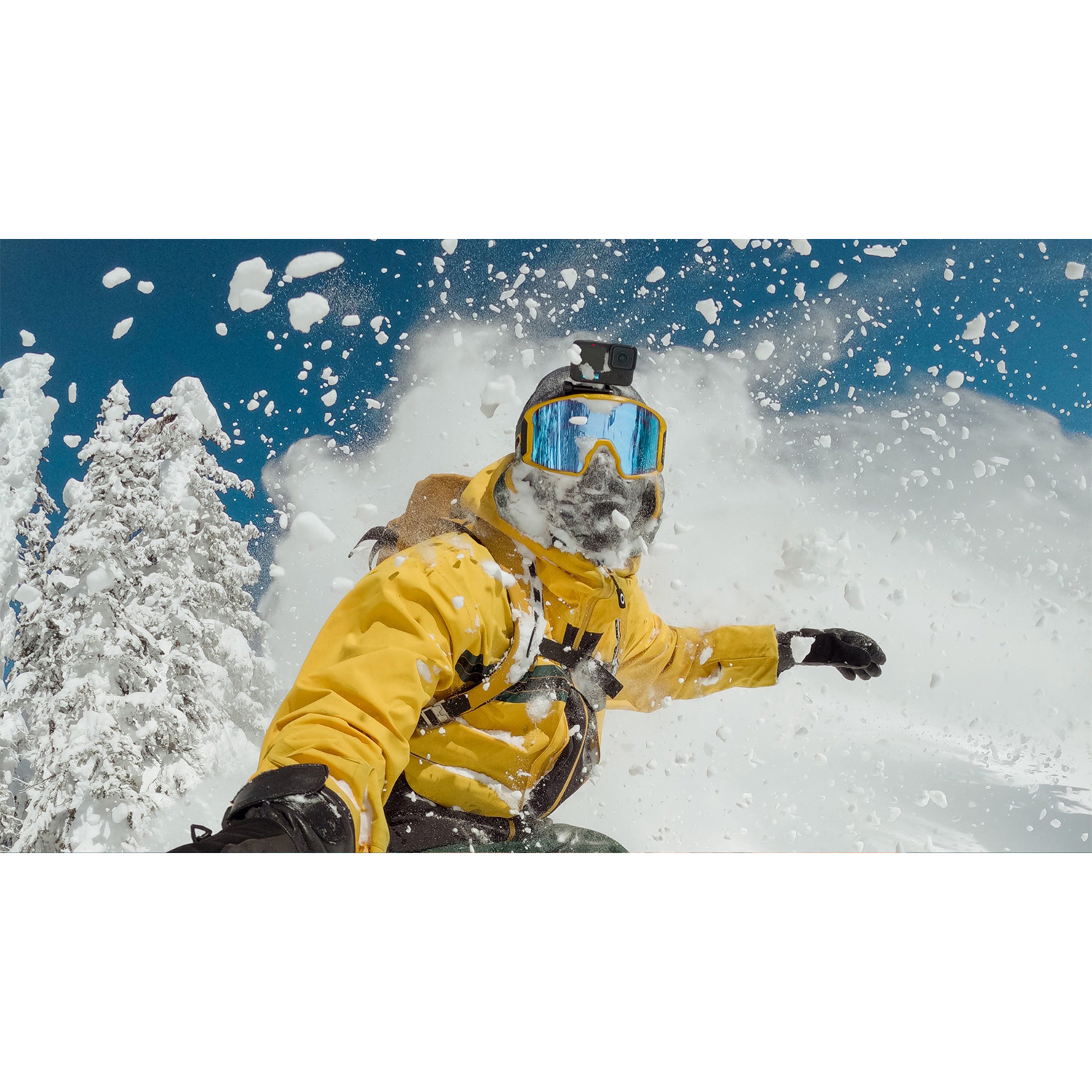 Snowboarder con giacca gialla, coperto di neve, con una GoPro sul casco.