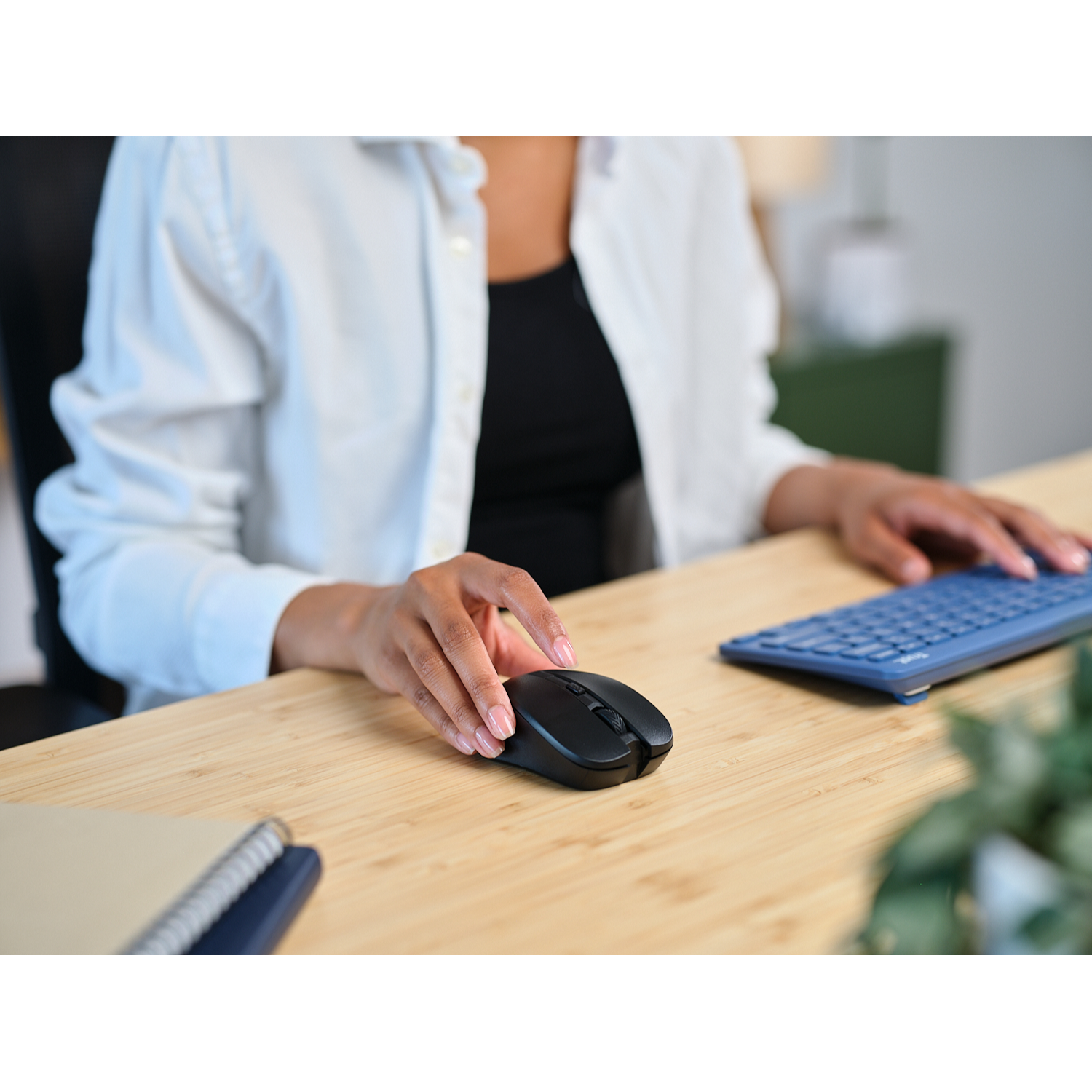Person using a black mouse on a wooden desk. A keyboard and notebook are also visible.