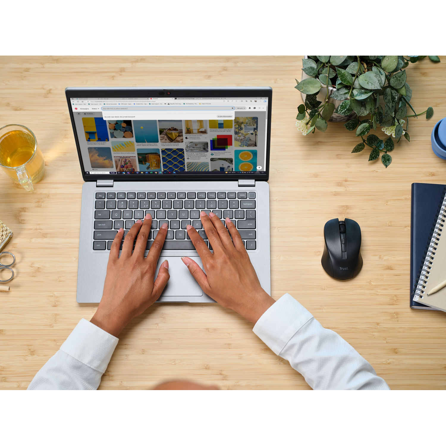 Hands typing on a laptop keyboard, next to a mouse, drink, and notebook.