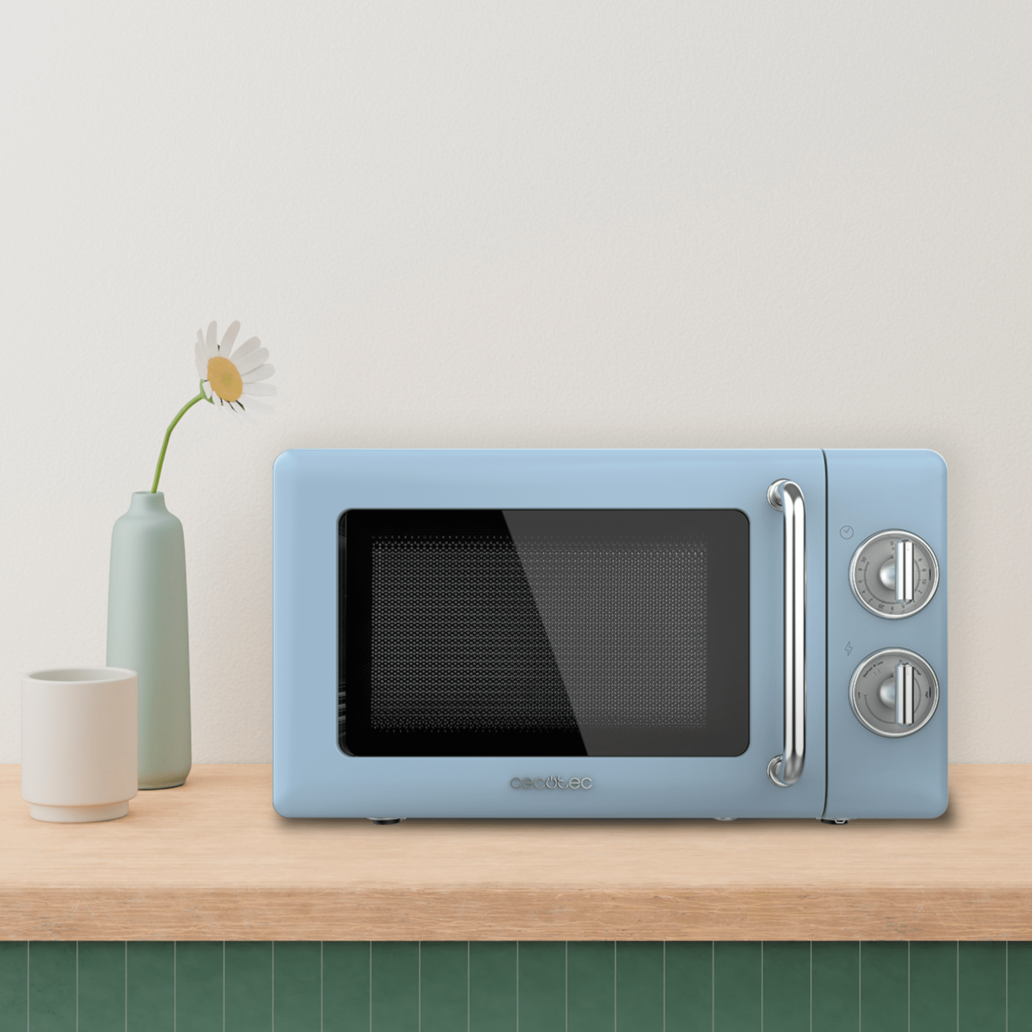 Un horno microondas azul sobre una mesa de madera con un jarrón de flores y una taza a un lado.