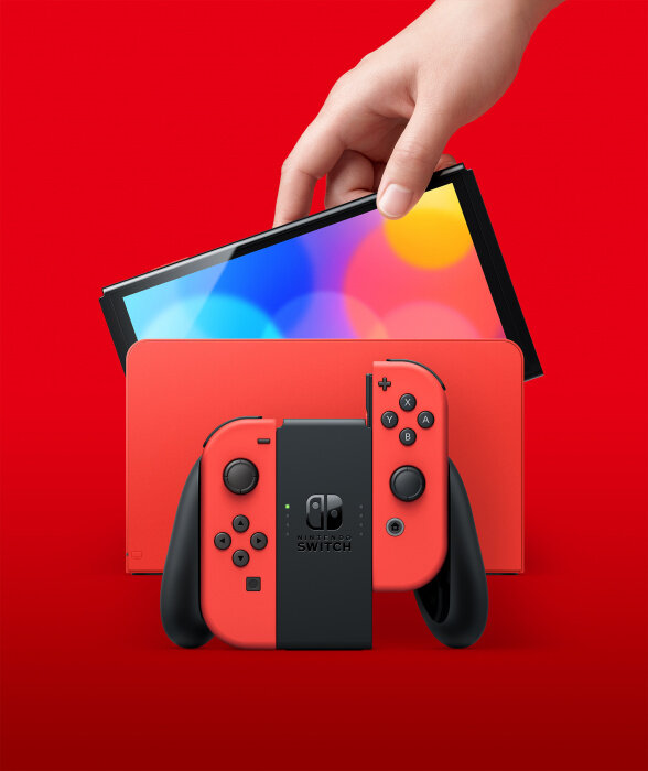 Czerwono-czarna konsola i kontrolery Nintendo Switch, wraz ze stacją dokującą, na czerwonej powierzchni.