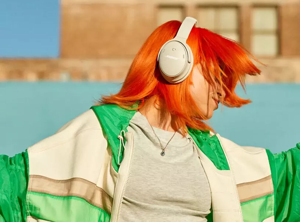 Femme aux cheveux oranges, casque blanc, veste verte, posant à l'extérieur.