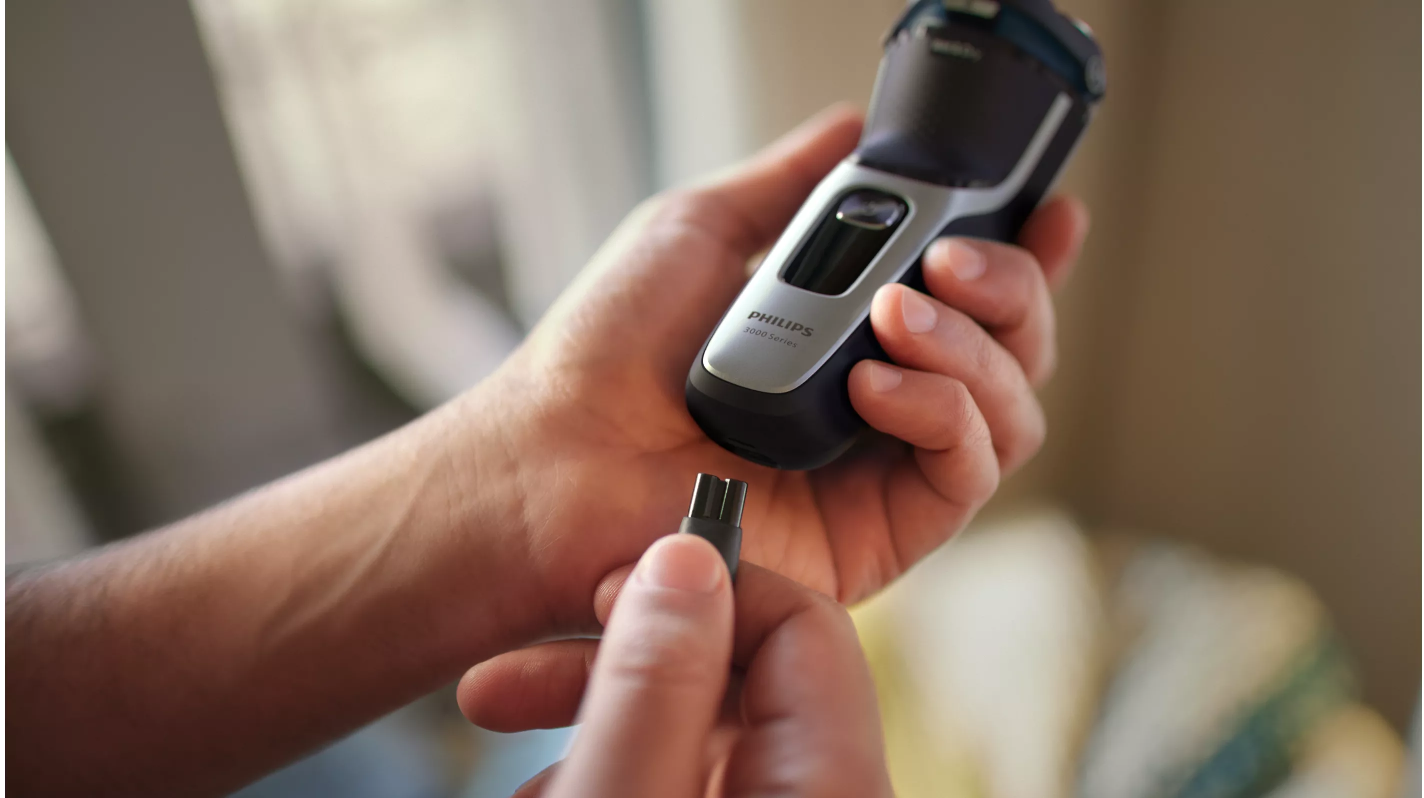 Les mains tiennent un rasoir Philips et un câble de charge. Le chargeur est débranché.