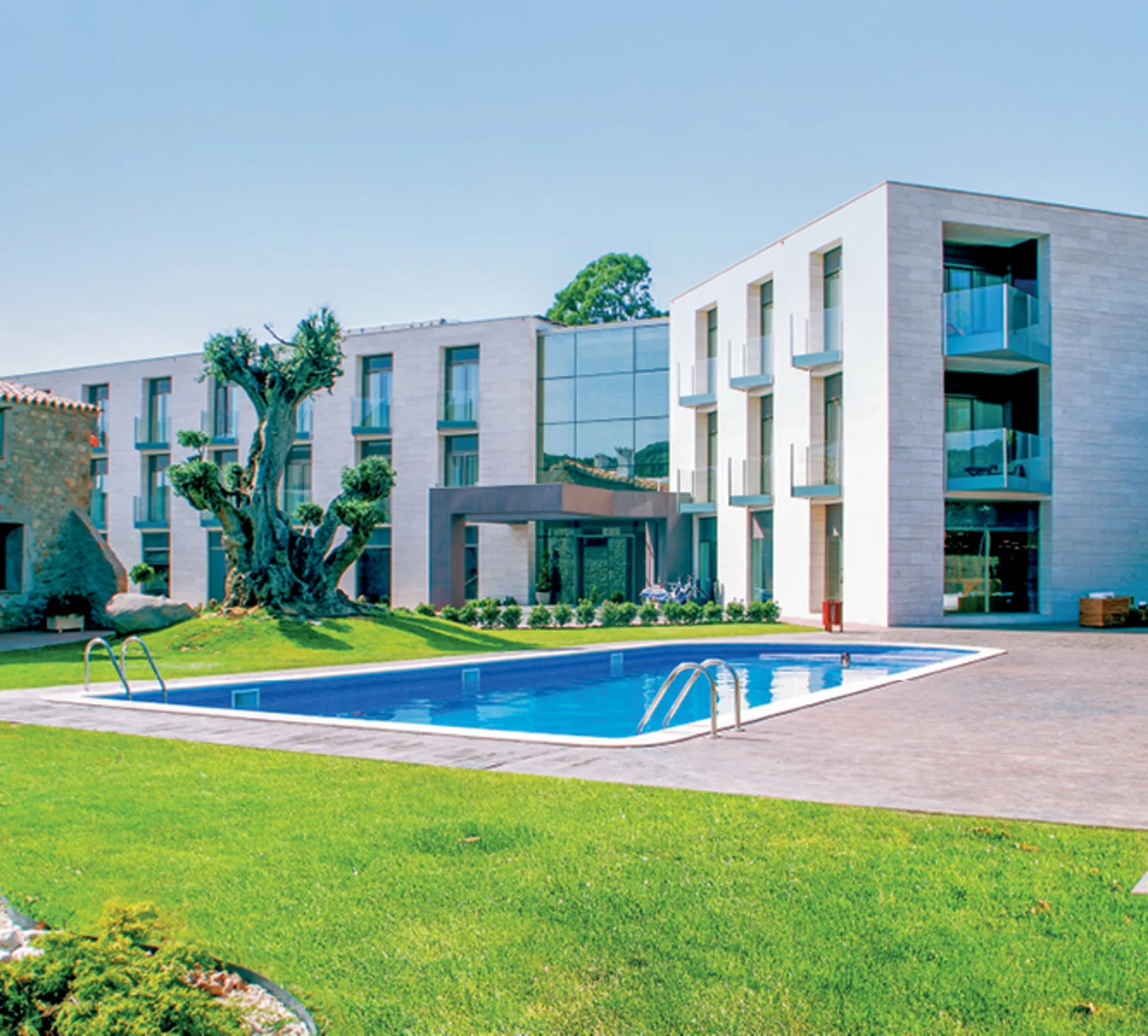 Un moderno edificio alberghiero bianco con piscina e prato verde.