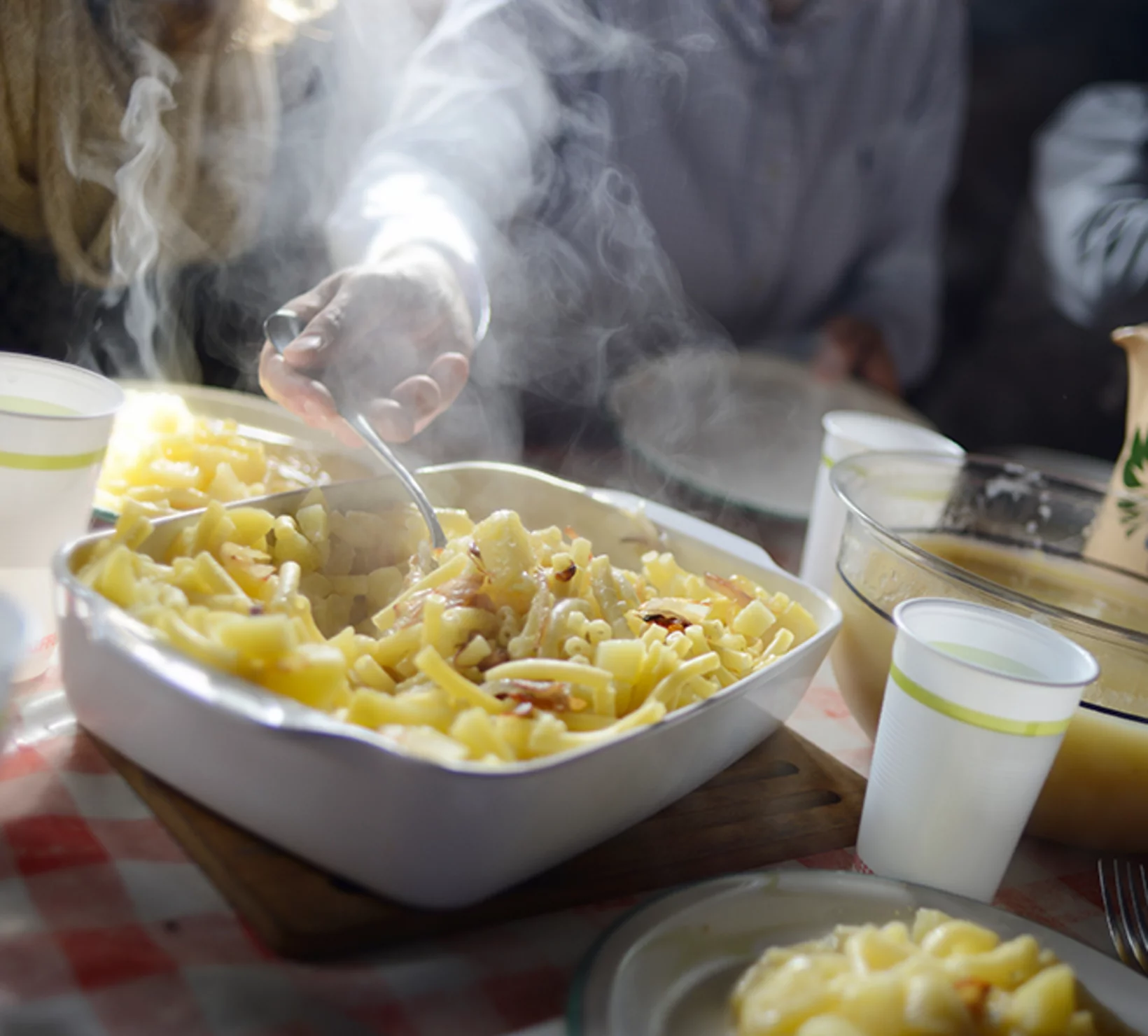 Una persona che serve un piatto di pasta con prosciutto e formaggio, con vapore che sale.