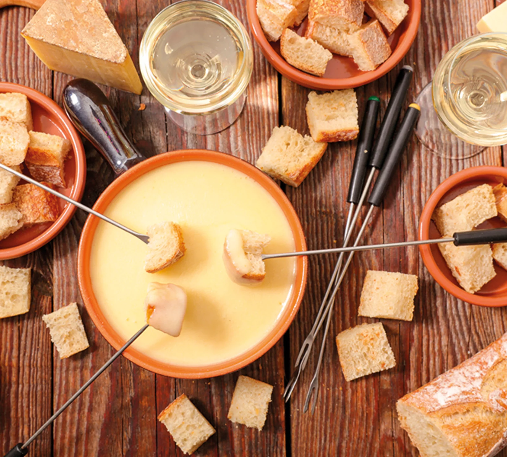 Una scena di fonduta con formaggio fuso in una pentola con pane e bicchieri di vino.