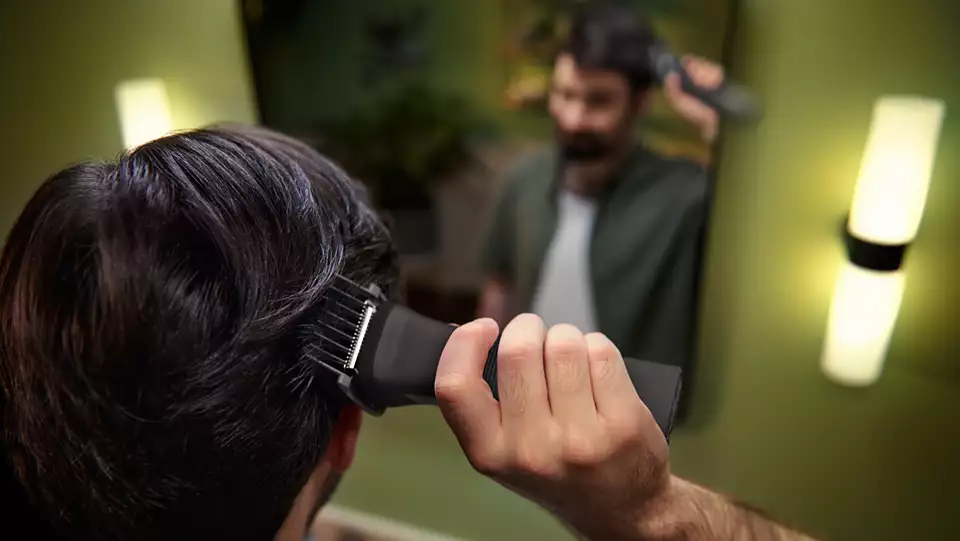 Un homme se coupe les cheveux avec une tondeuse devant un miroir.