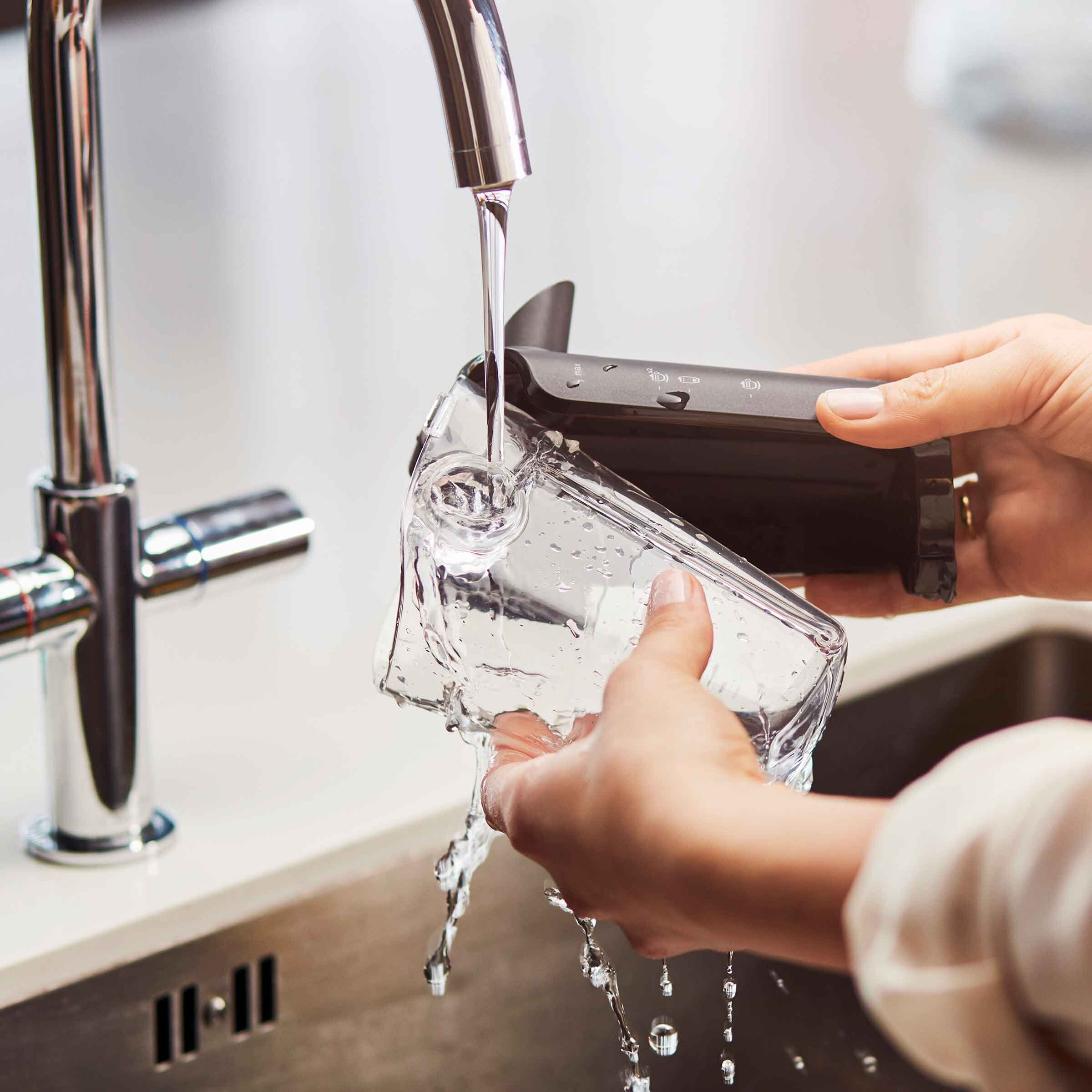 Ręce myjące przezroczysty pojemnik pod kranem w zlewie kuchennym, woda się rozpryskuje.