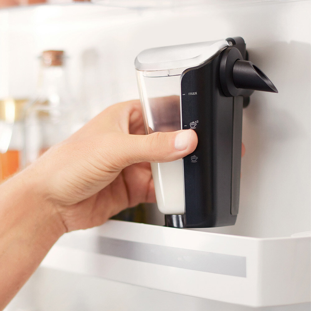 Dłoń trzymająca pojemnik na mleko w lodówce. Pokazuje maksymalny poziom.