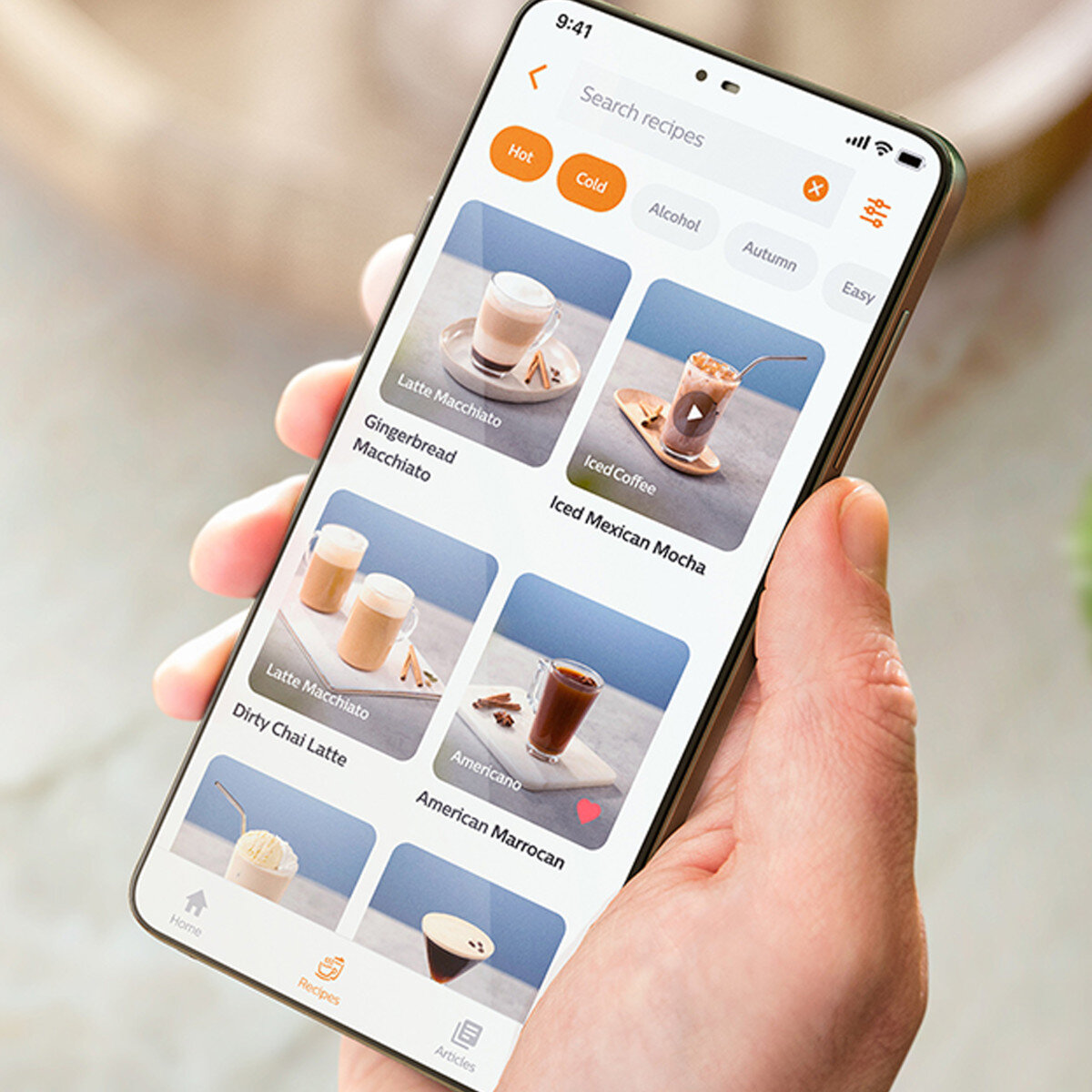 Dłoń trzymająca telefon wyświetla aplikację z przepisami na kawę.