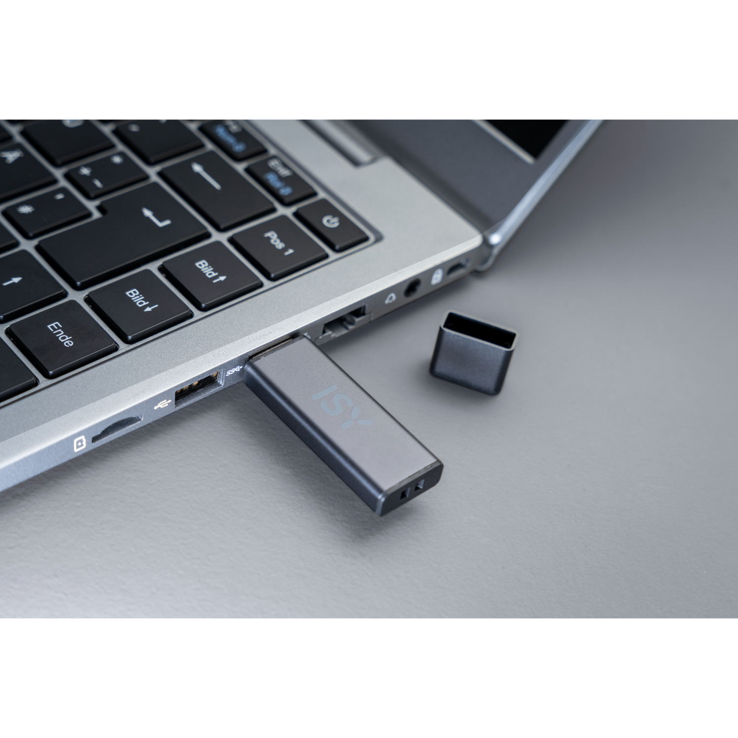 Een USB-stick aangesloten op een laptop. De stick heeft 'ISY' erop gedrukt, grijs oppervlak.