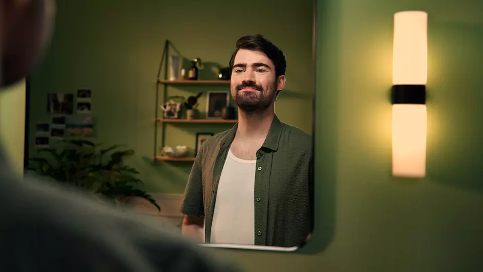 Un uomo si guarda allo specchio, con una stanza dai toni verdi e una luce.