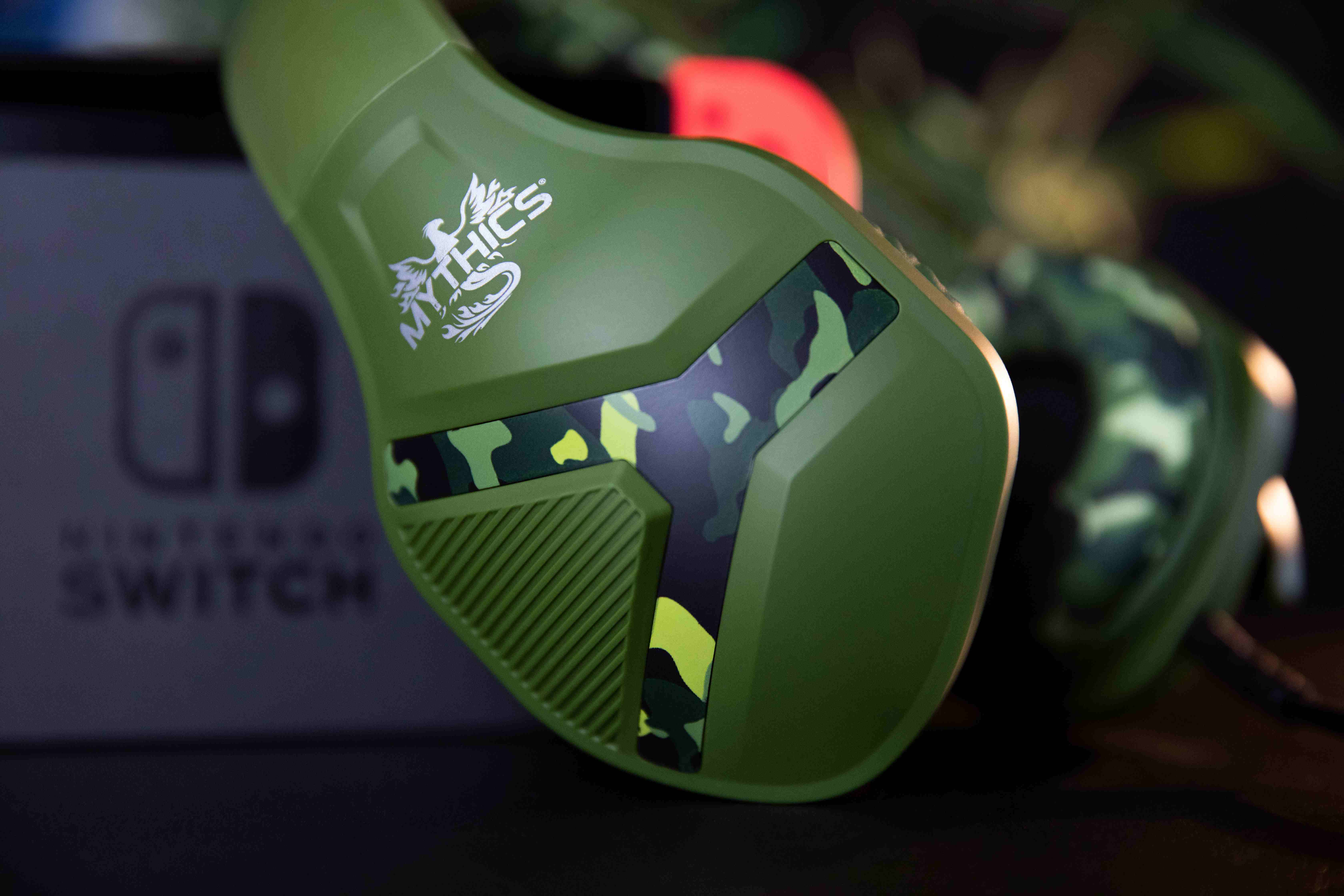 Grünes Gaming-Headset mit Camouflage-Muster und Nintendo Switch im Hintergrund.
