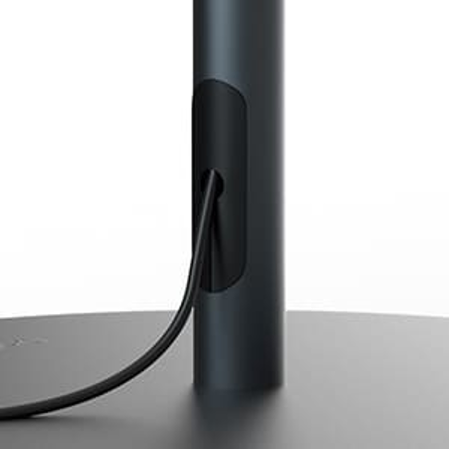 Ein schwarzes Kabel kommt aus der Rückseite eines dunkelgrauen Monitorständers. Der Ständer steht auf einer hellgrauen Oberfläche.