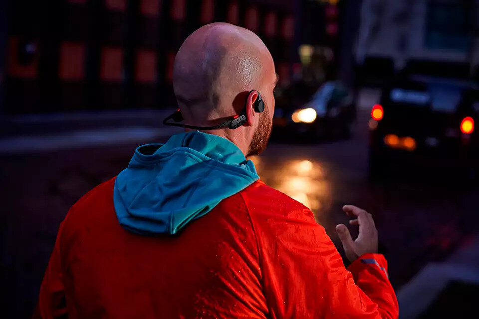 Biegacz w czerwonej kurtce i słuchawkach. Scena nocna, rozmyte tło.