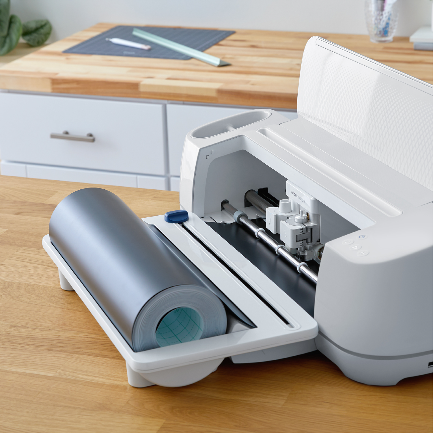 White cutting machine with a roll of grey material. It is on a wooden table.