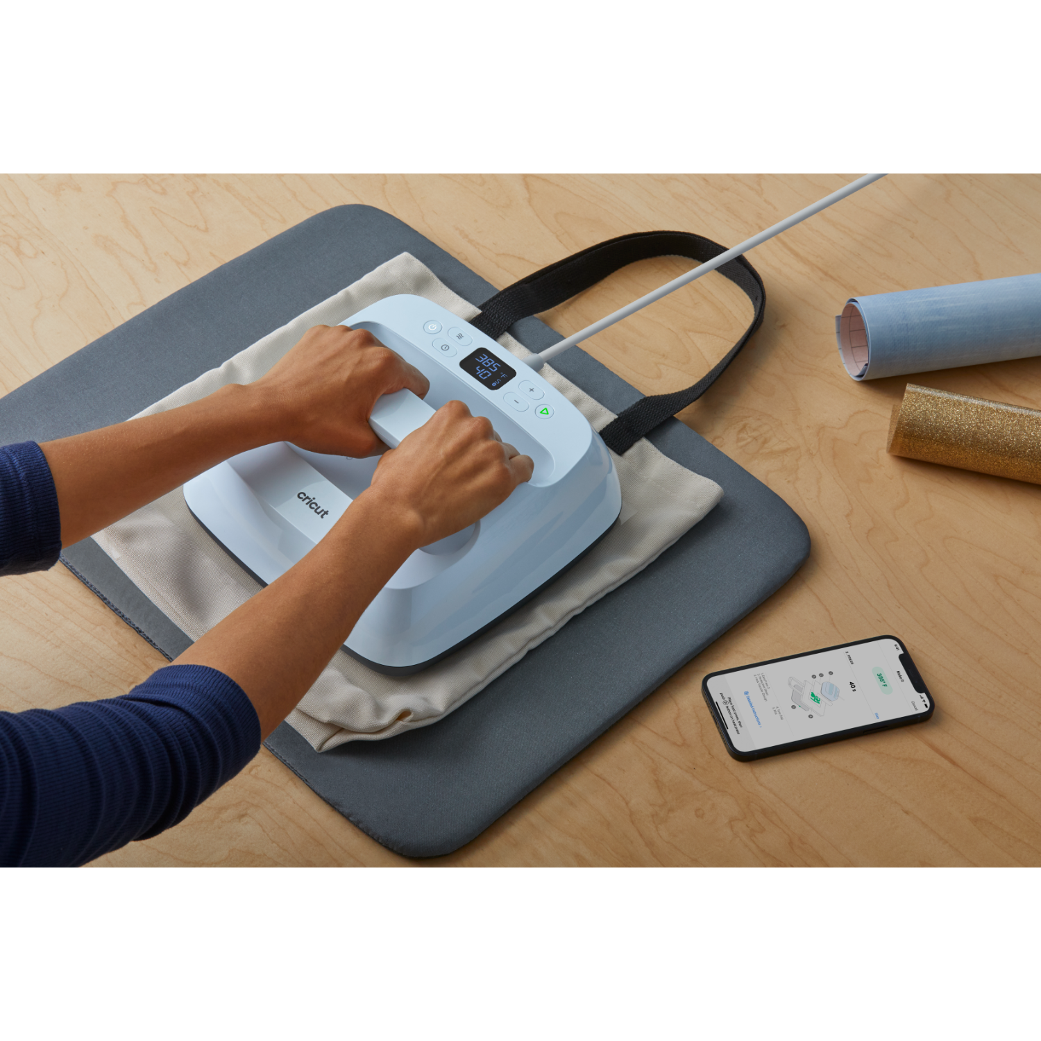 Person using a light blue heat press with a tote bag on a wooden table.