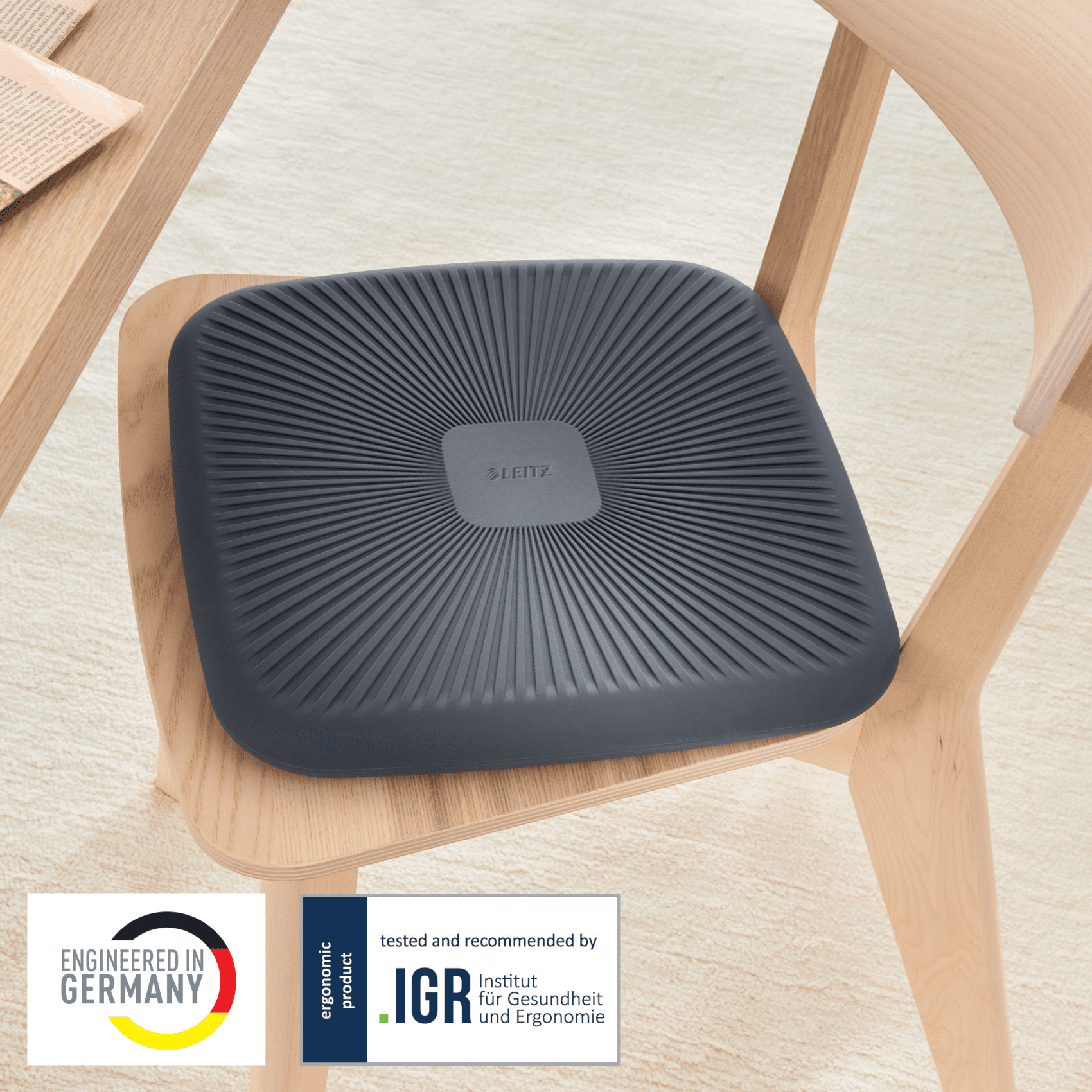 Sötétszürke ergonomikus ülőpárna egy fa széken. A párna textúrázott felületű.