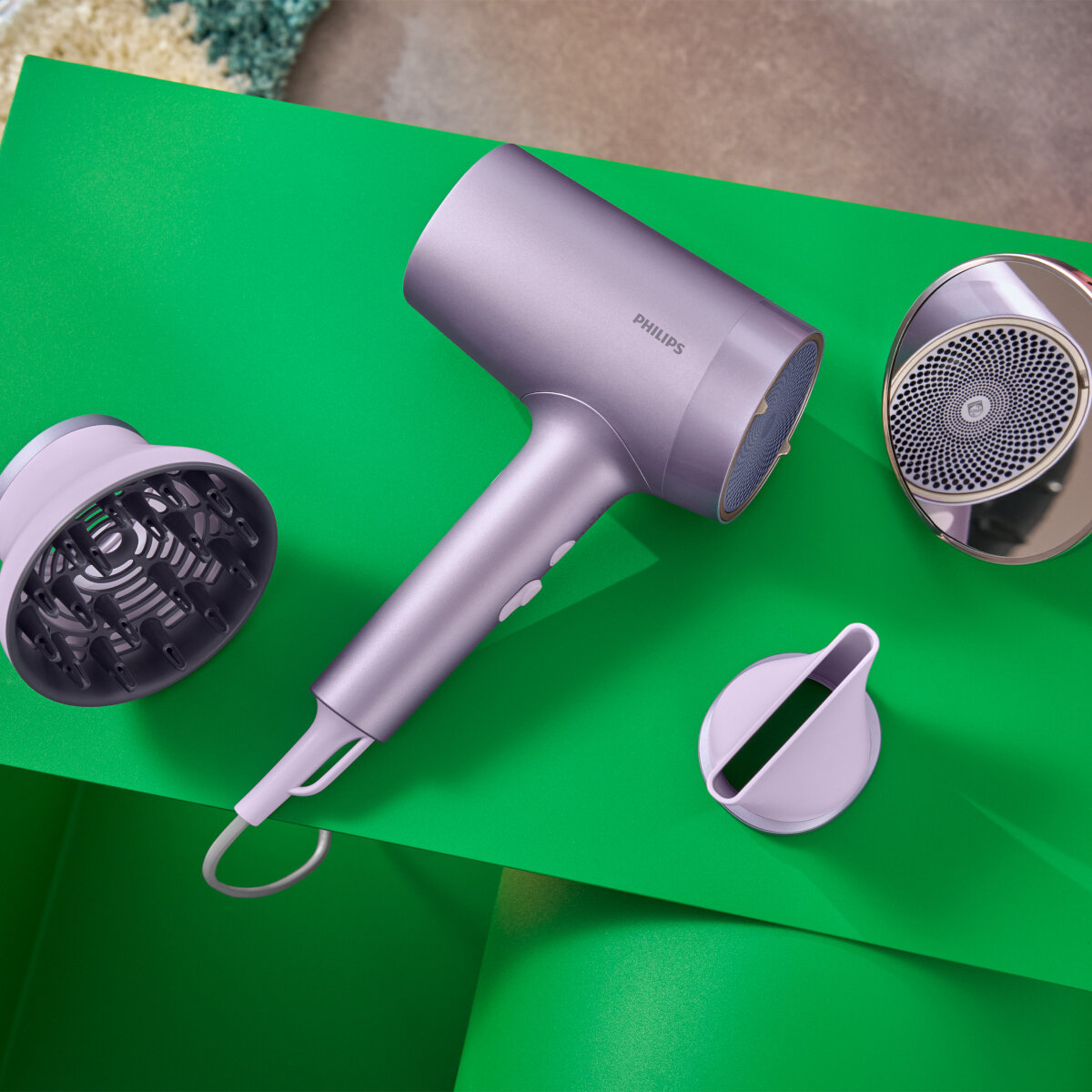 Suszarka do włosów, dyfuzor i koncentrator na zielonej powierzchni. Suszarka jest fioletowa.
