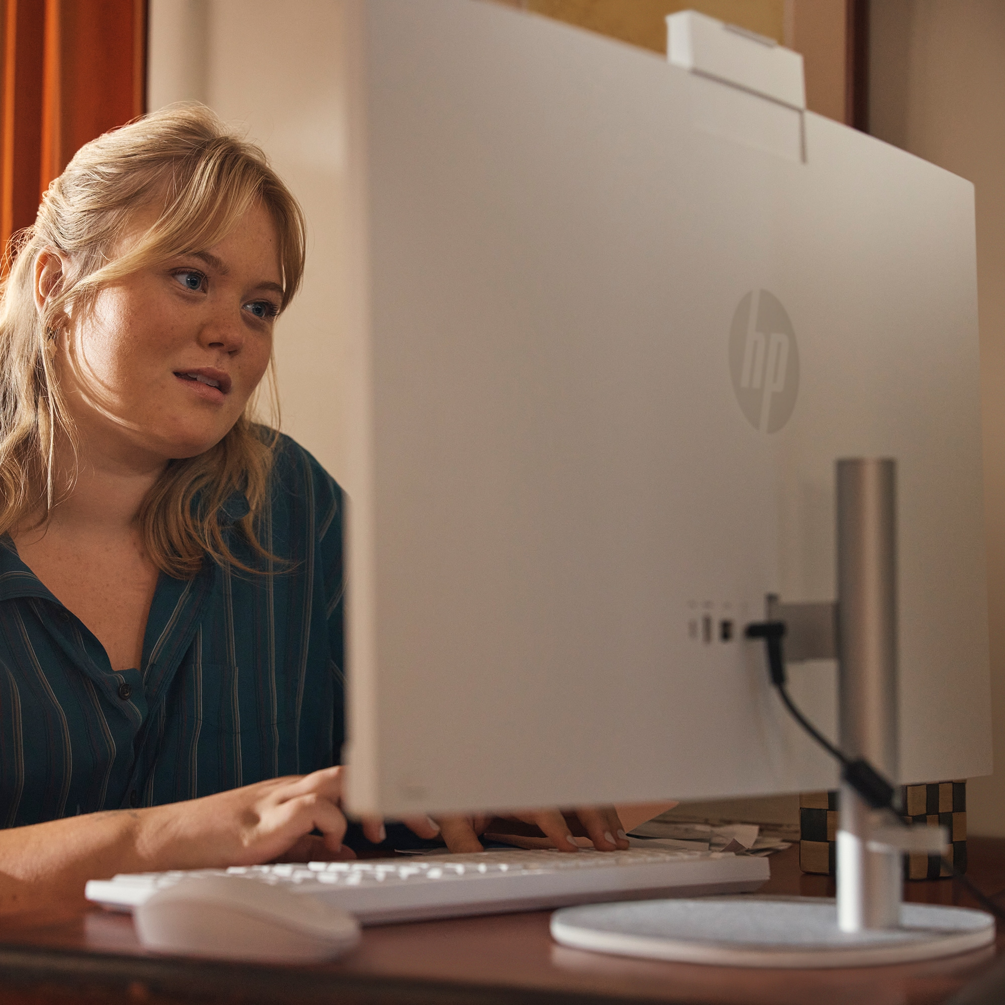 Blonde Frau benutzt einen weißen Computer. Tastatur und Maus im Fokus. HP-Logo auf dem Bildschirm.