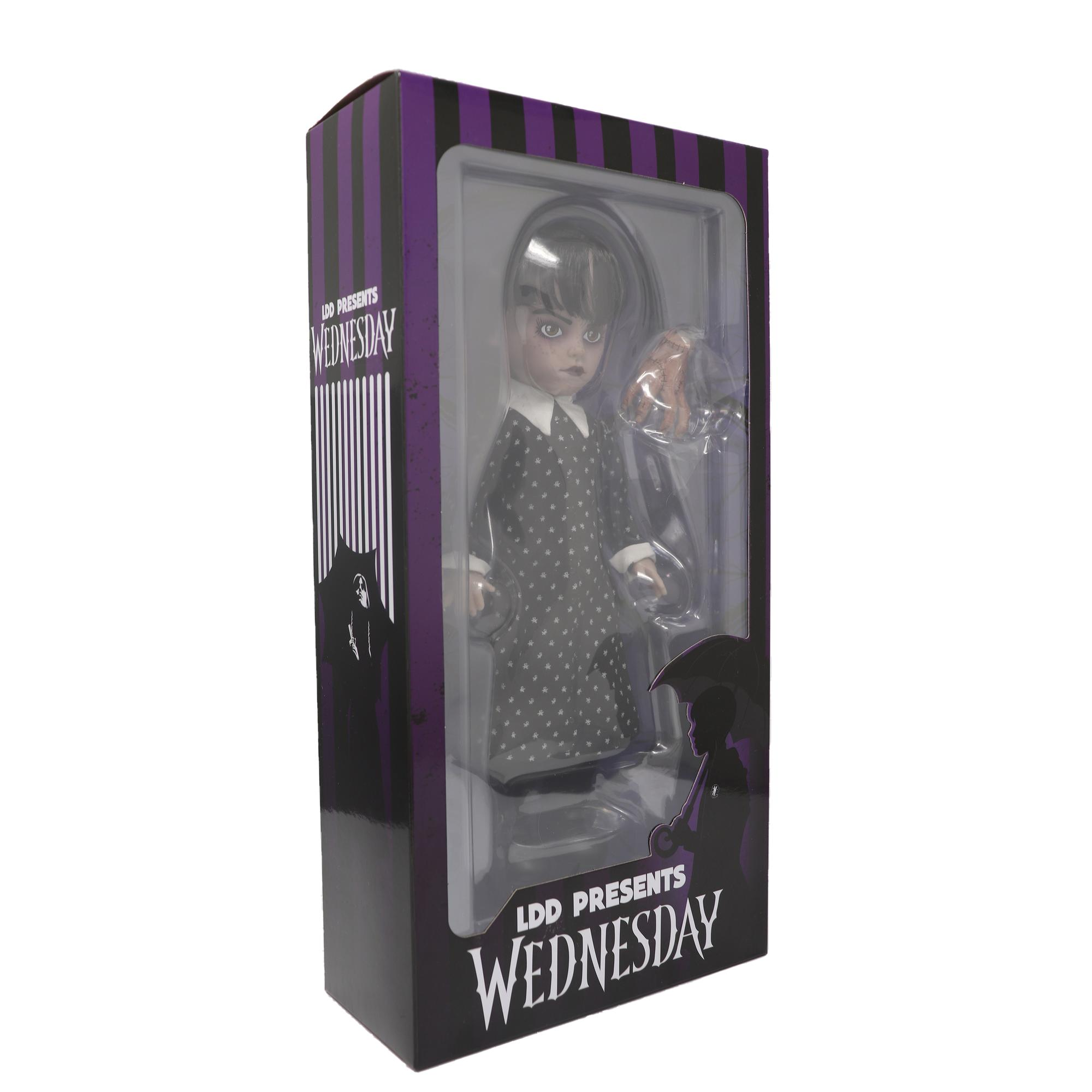 Eine Wednesday Addams Puppe in einer Box. Sie trägt ein schwarzes Kleid mit weißen Punkten und hält eine Hand.