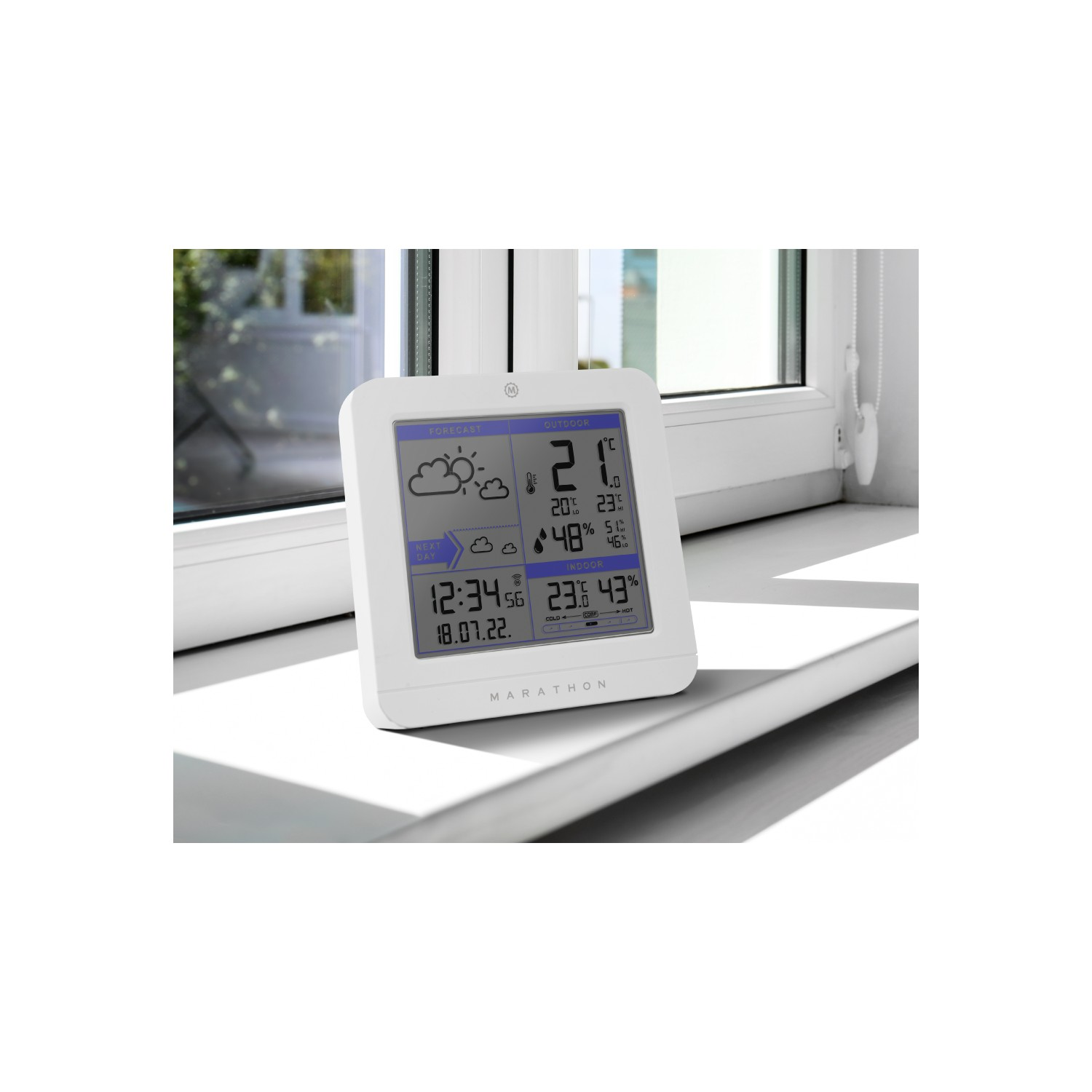 White weather station on a windowsill showing the time, date, and weather forecast.