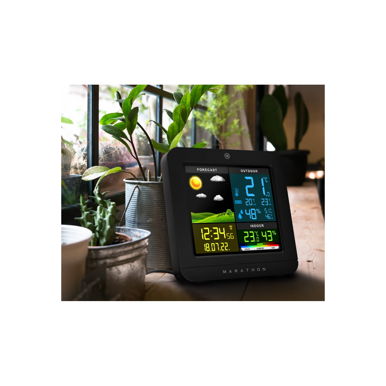 Weather station on a wooden table with plants by a window. Displays weather info.