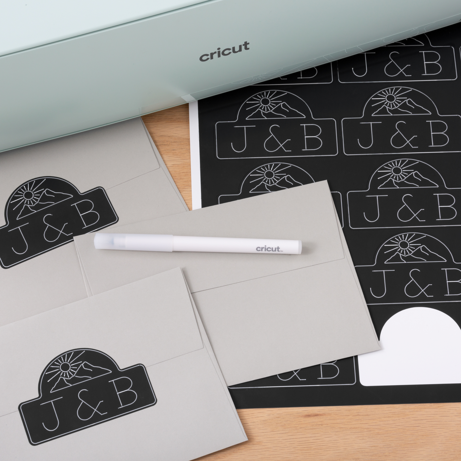 Craft supplies: a Cricut machine, envelopes, and a pen. Envelopes have a logo.