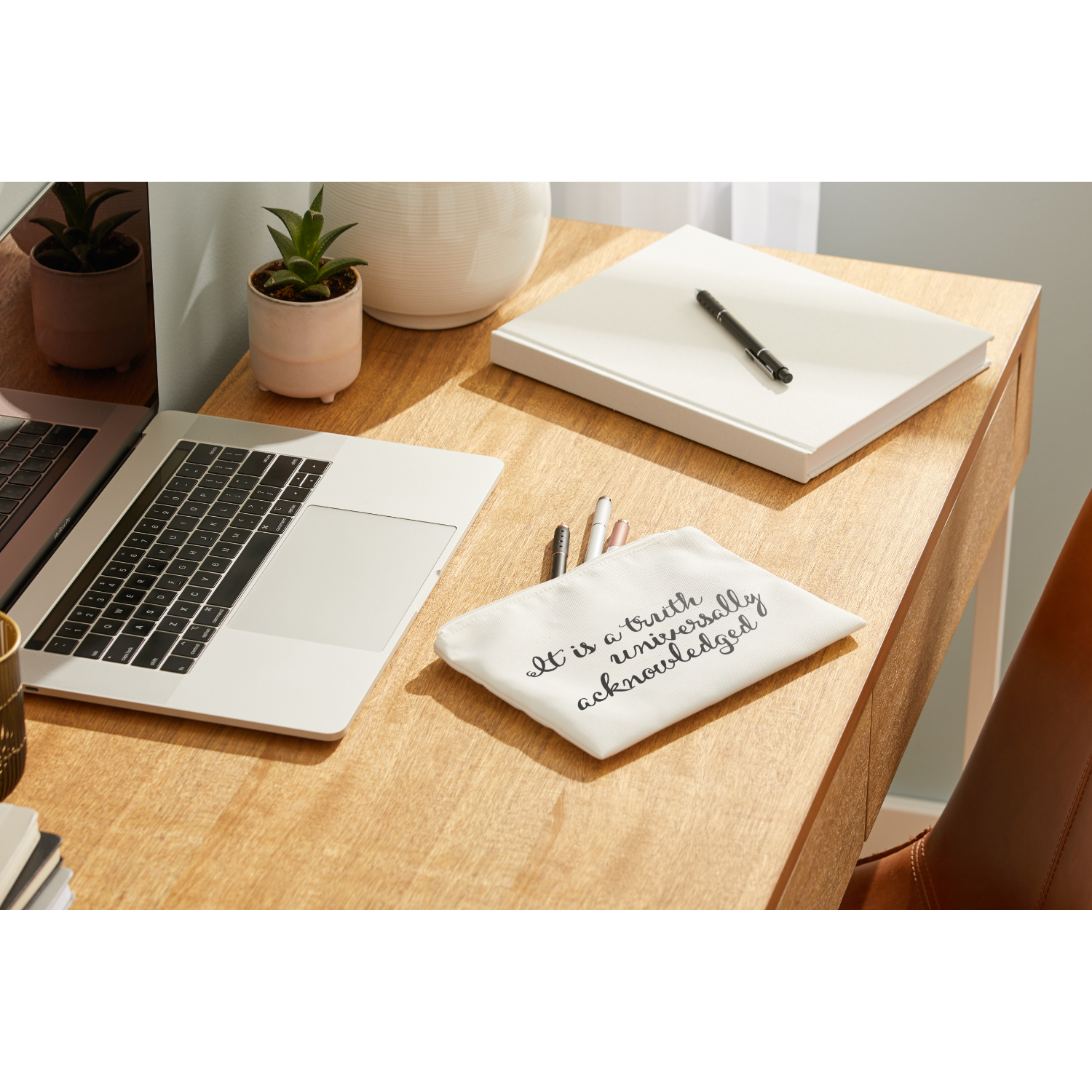 Bureau met laptop, notitieboek, pen en een kleine tas met tekst.