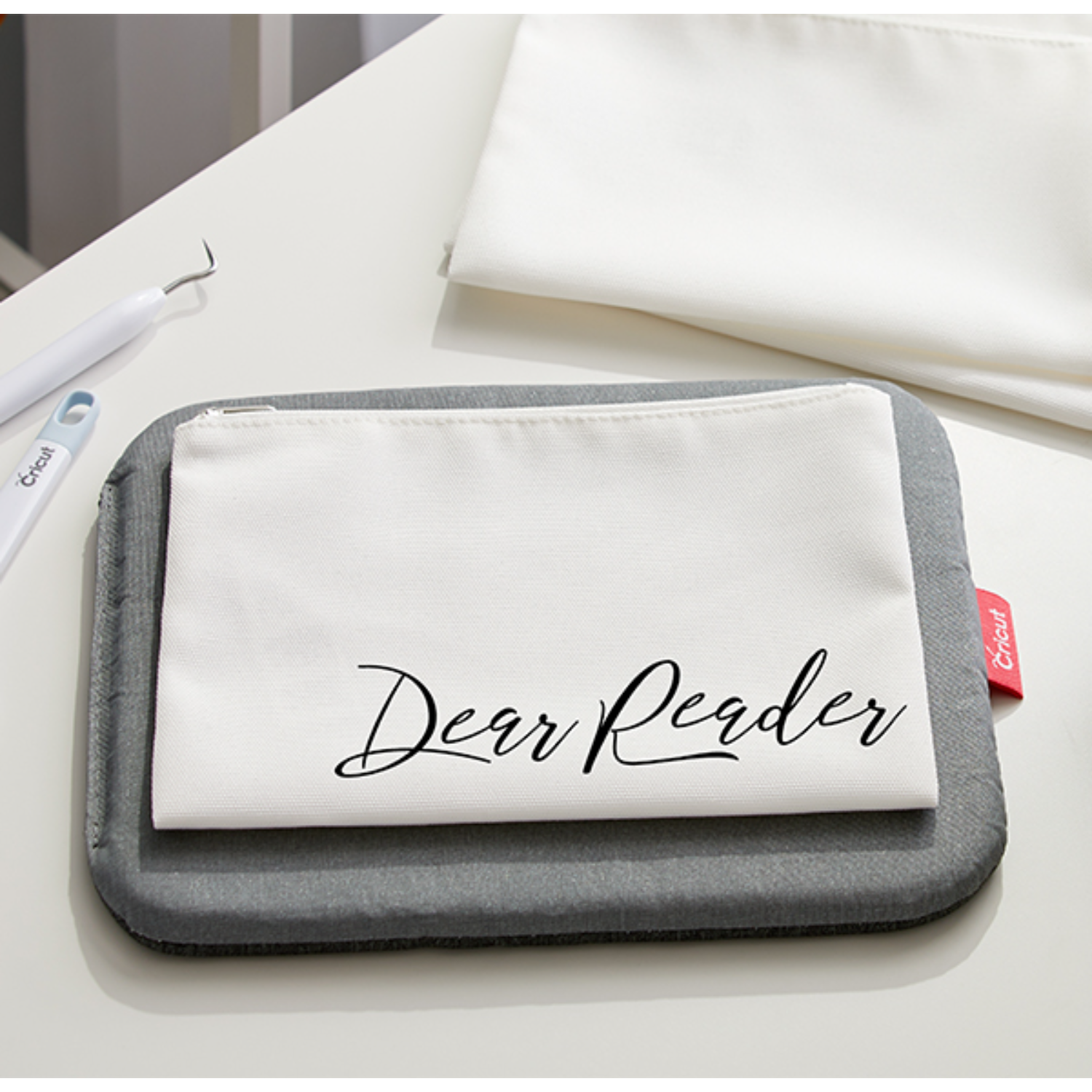 Een witte canvas etui op een grijze Cricut pad met de woorden 'Dear Reader' in zwart geschreven.