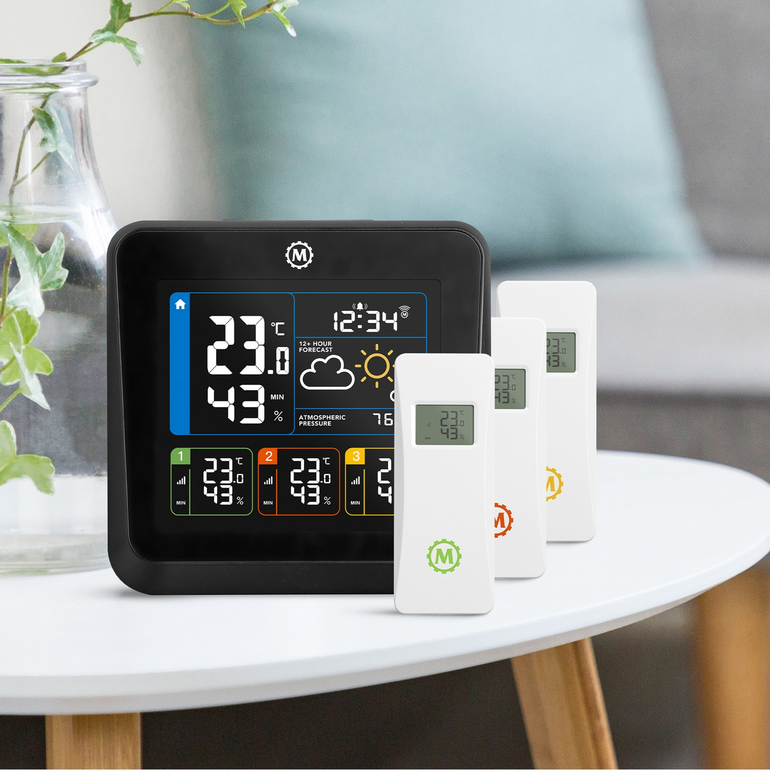 Black weather station with display and three white remote sensors on a table.