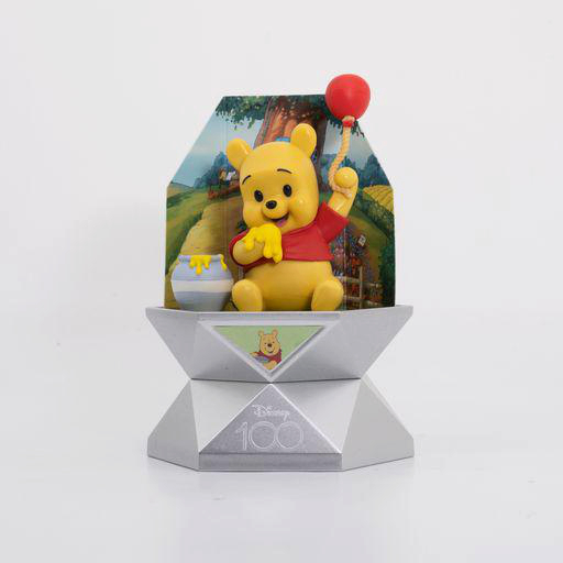 Winnie-the-Pooh-Figur auf einem Podest. Er hält einen Ballon. Der Hintergrund ist eine Waldszene.