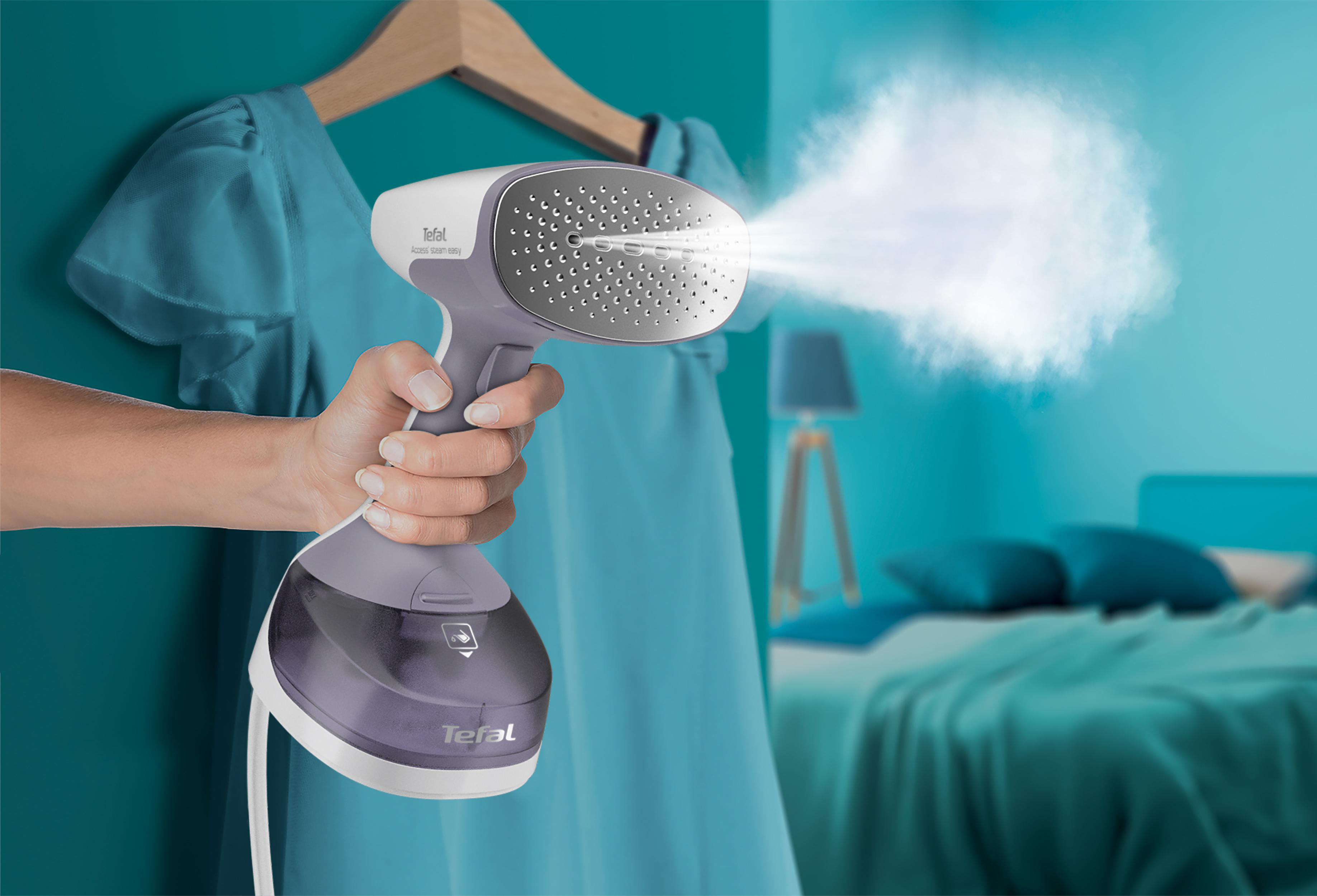 Person hält einen grau-violetten Steamer mit Dampf. Blaues Kleid im Hintergrund.