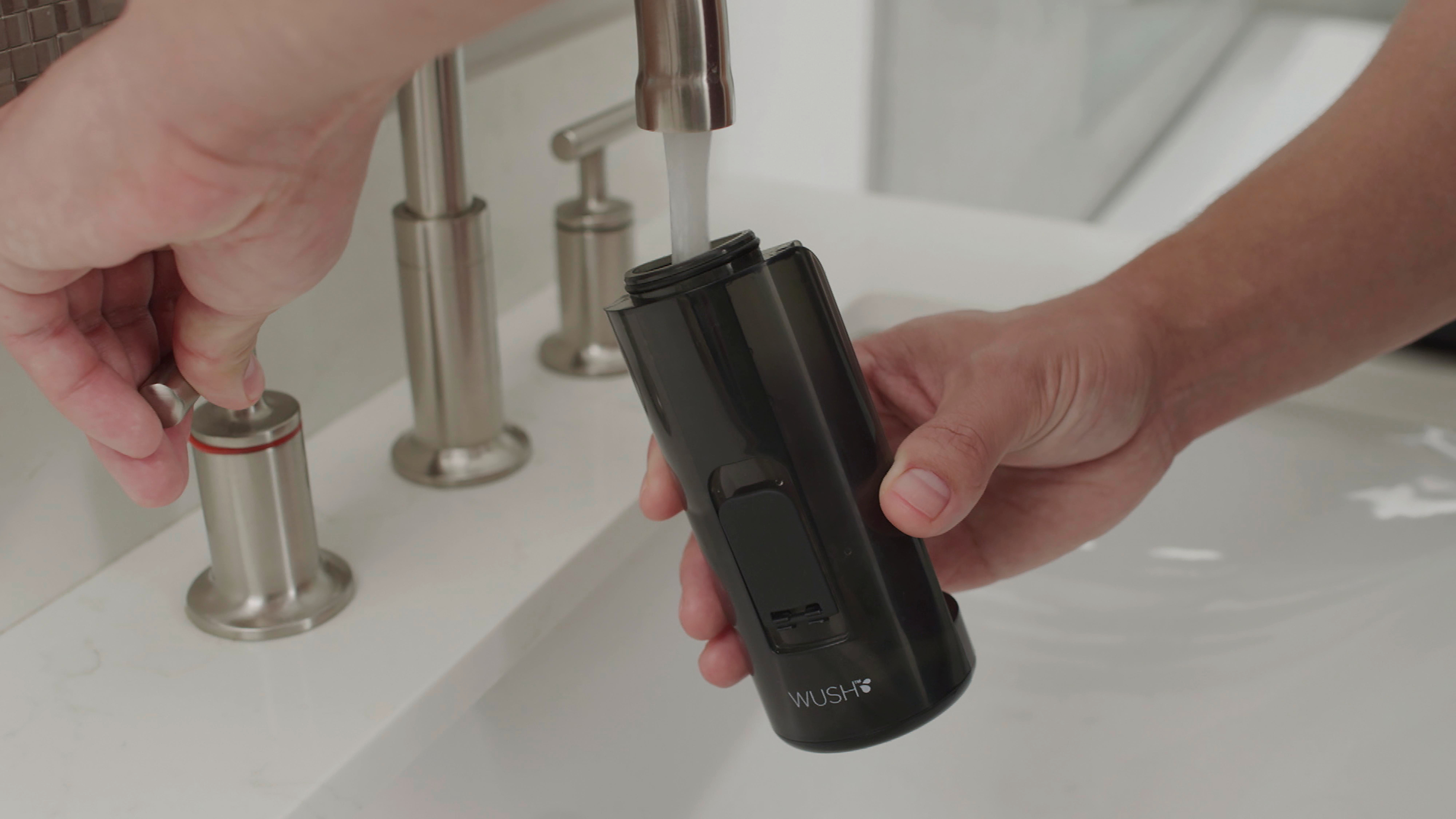 Eine Person füllt ein schwarzes WUSH-Gerät mit Wasser am Waschbecken.