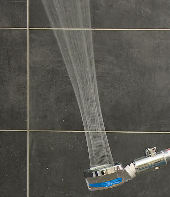 Duschkopf mit fließendem Wasser, vor einer schwarzen Fliesenwand.
