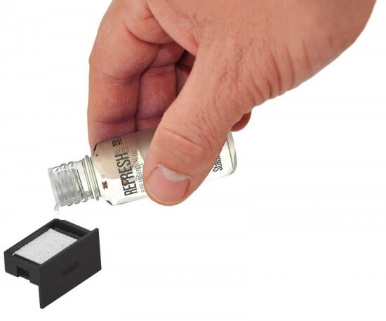 Ręka wlewa ciecz z butelki do czarnego pojemnika.