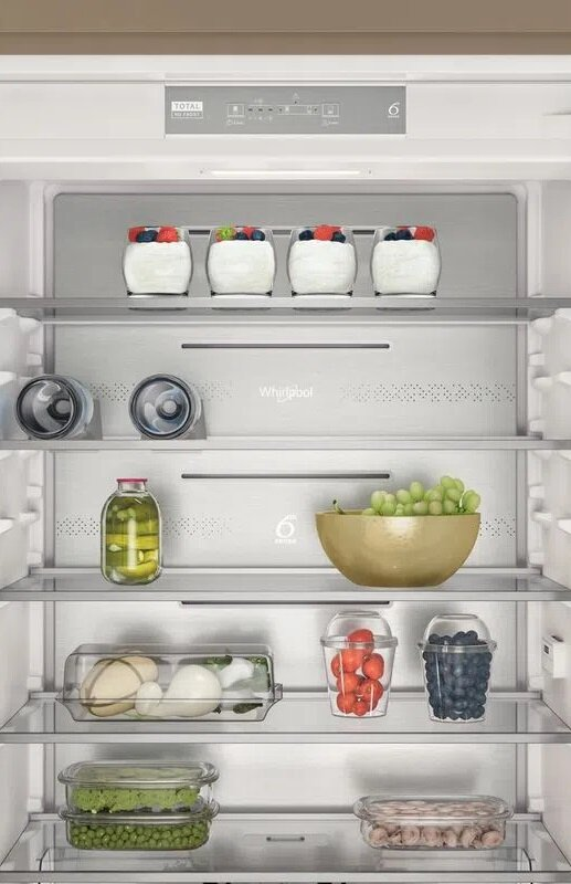 Otwarta lodówka ze słoikami, butelkami i świeżymi produktami na półkach.