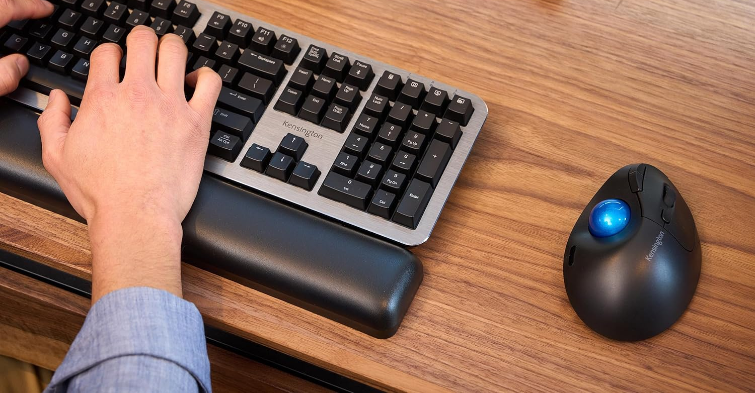 Kéz a billentyűzeten gépel, jobb oldalon trackball egér, fa asztal.