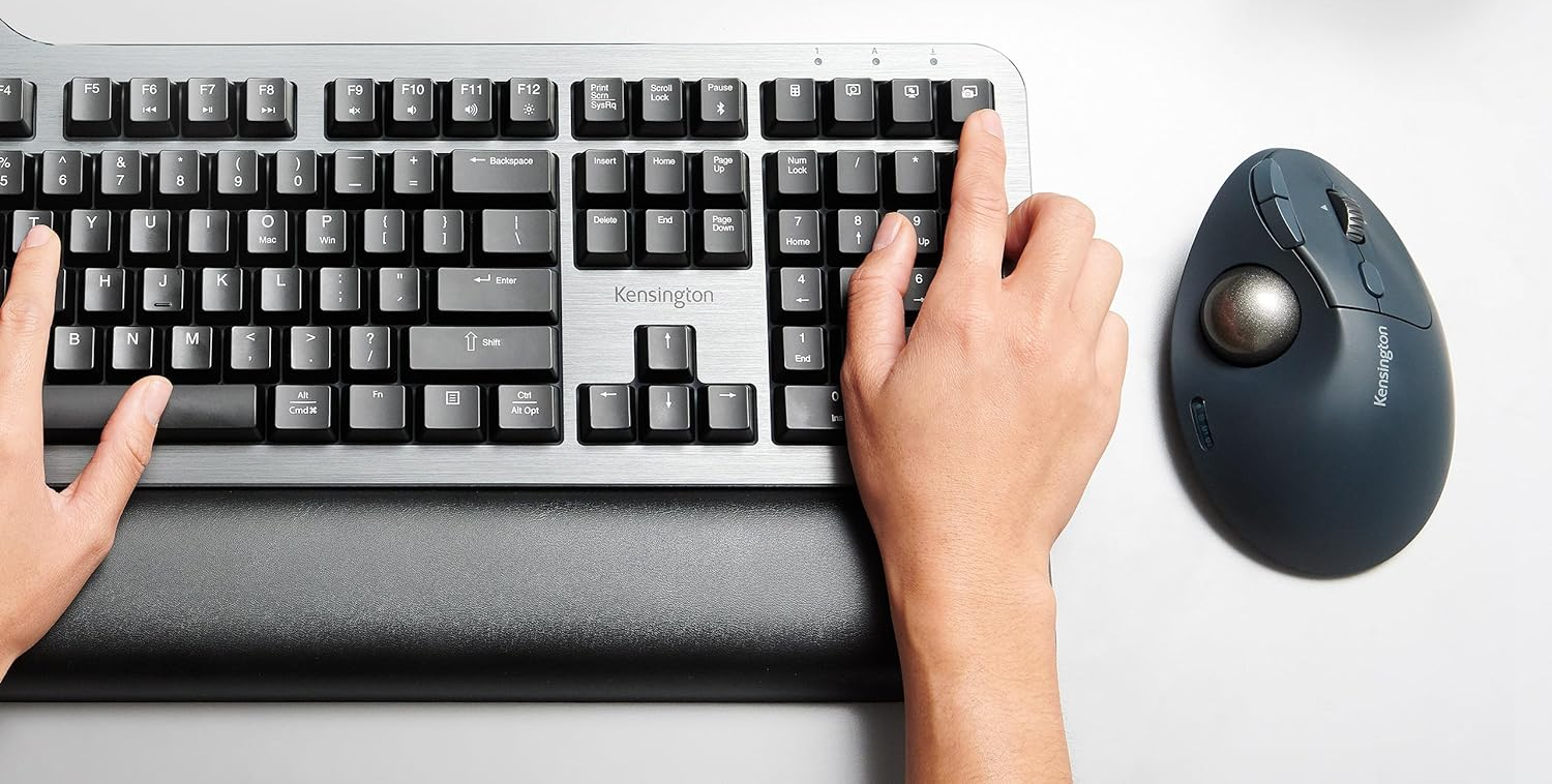 Kéz a billentyűzeten és ergonomikus egéren. Az egér szürke és trackballja van.