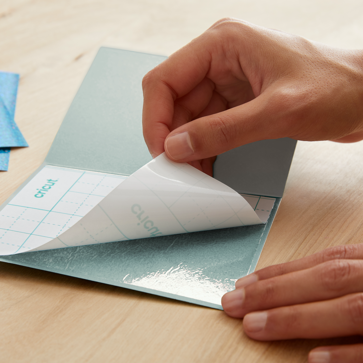 Hand peeling a white sheet from a blue sticker sheet on a wooden table.