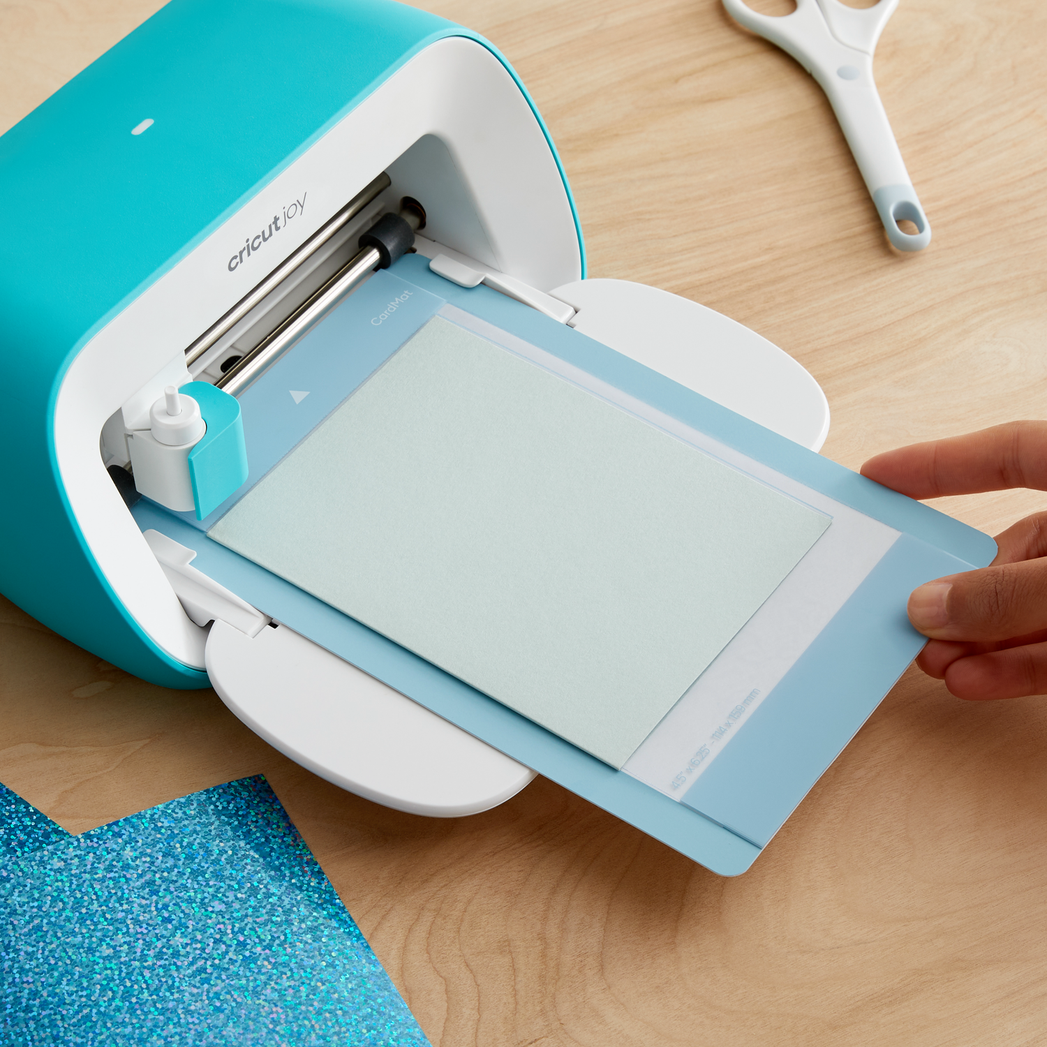 Cricut Joy machine with a hand placing a light blue cutting mat with paper into the machine.